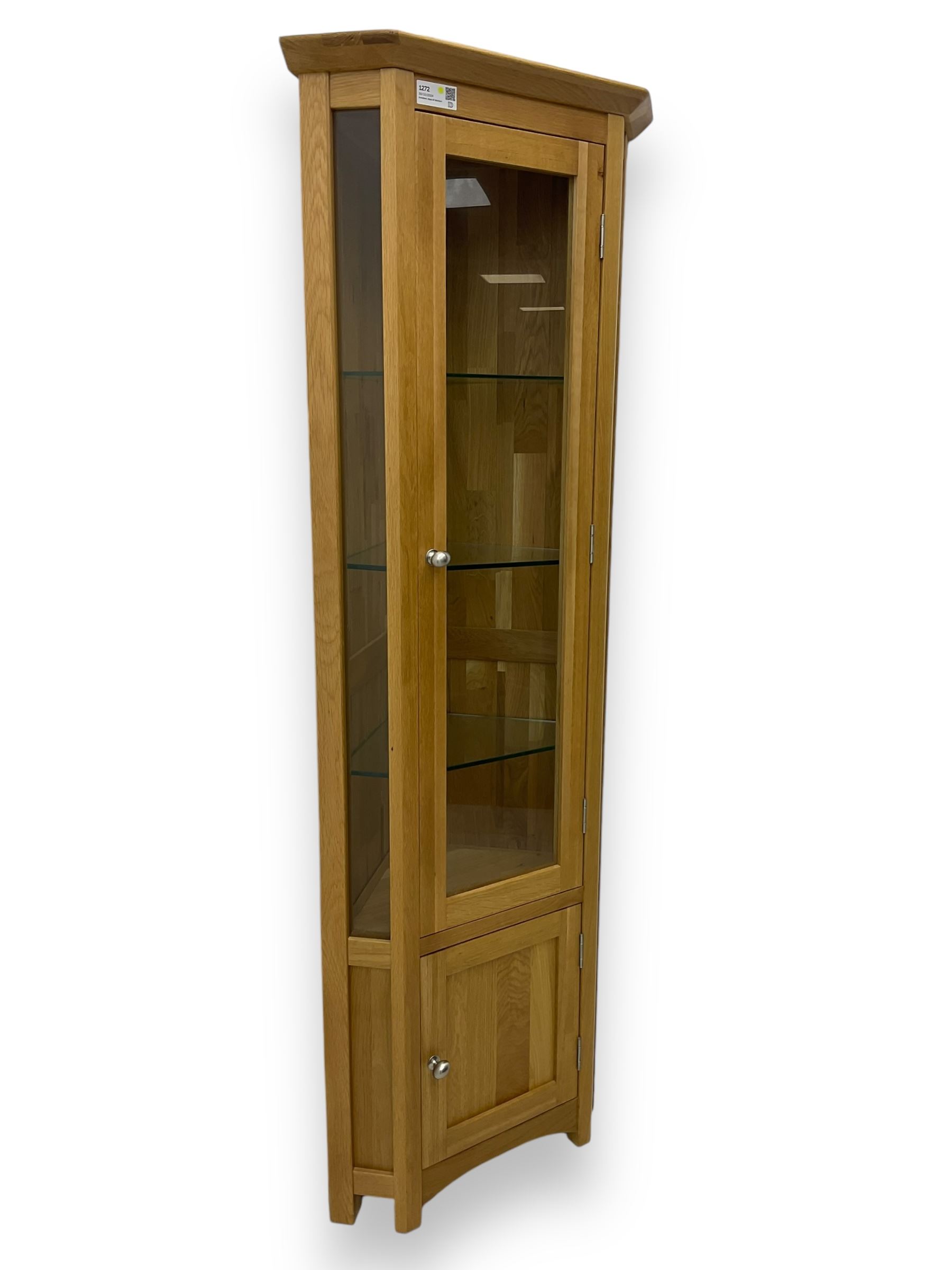 Contemporary light oak corner display cabinet, projecting cornice over single glazed door enclosing three glass shelves, the base fitted with panelled cupboard enclosing single oak shelf, on stile supports