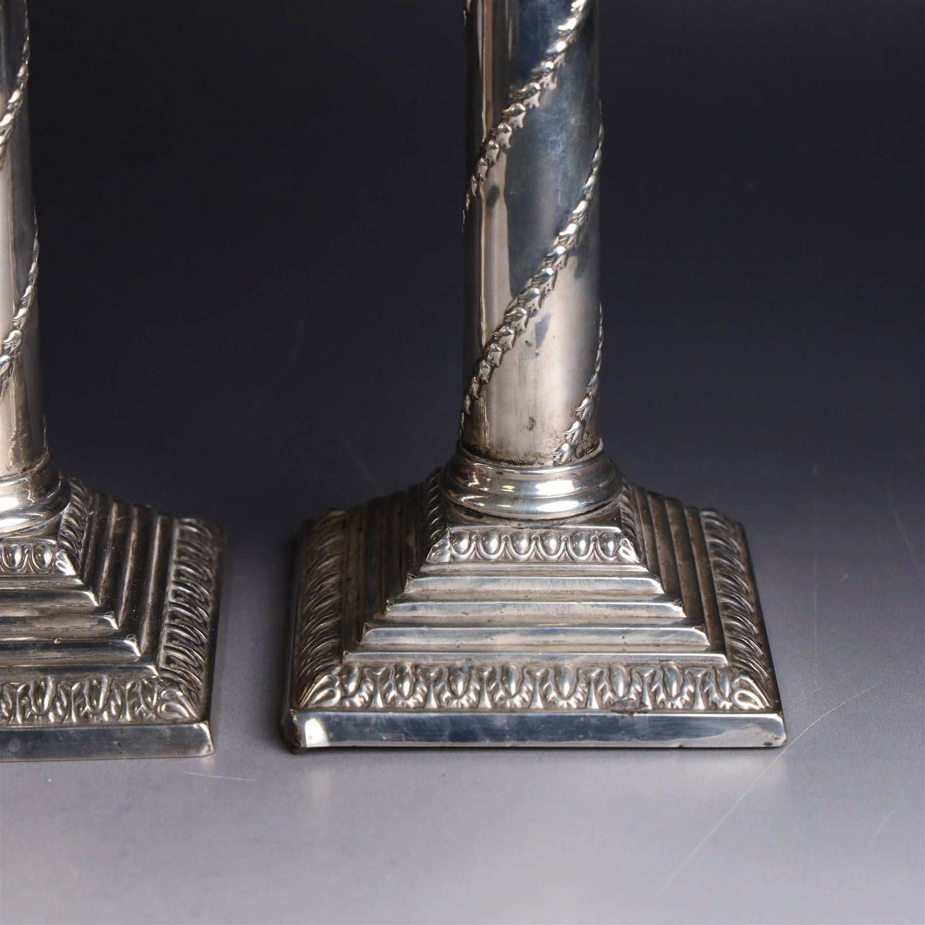 Pair of Edwardian silver mounted column candlesticks, each with embossed floral, foliate and scrolling decoration and upon stepped square weighted bases, hallmarked William Hutton & Sons Ltd, London 1901, H19cm