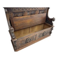19th century heavily carved oak settle, the moulded upper rail over triangular foliage carved frieze, three Flemish style carved panels depicting tavern scenes, acanthus carved uprights terminating to lion carved arms, hinged box seat, the panelled front carved with lion masks and extending scrolled acanthus leaves, on moulded skirt base
