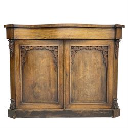 William IV rosewood serpentine chiffonier, fitted with frieze drawer over two panelled cupboard doors with applied C-scroll decoration, flanked by canted uprights with moulded foliate corbels