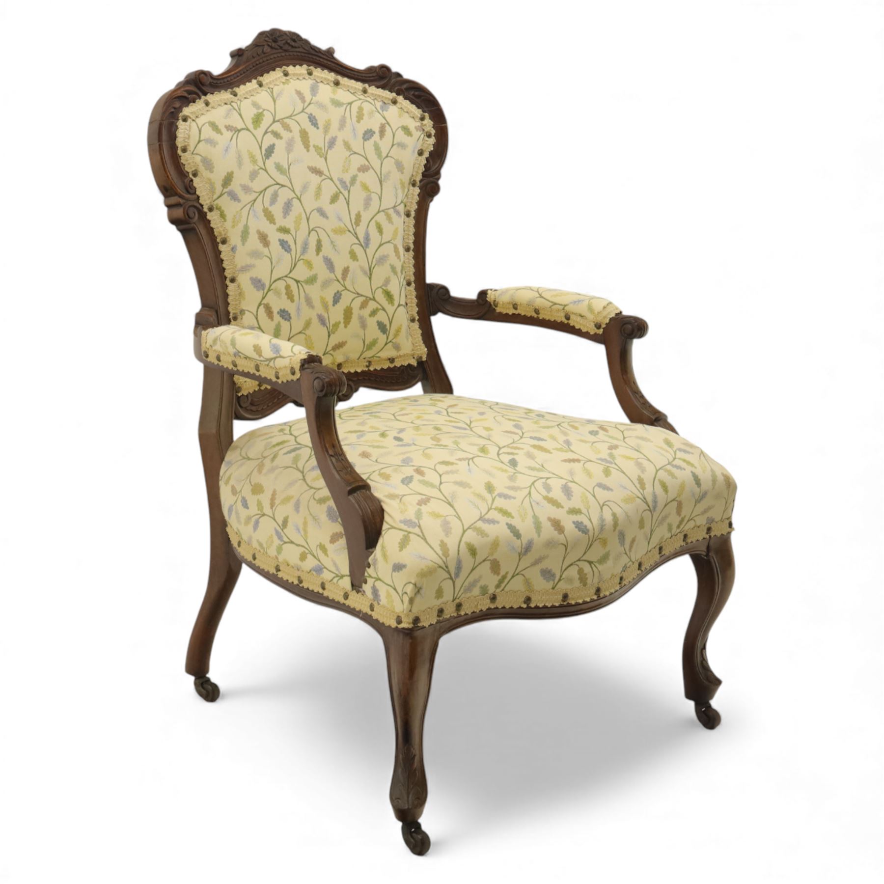 Victorian mahogany framed upholstered armchair, shaped and scroll carved cresting rail above a padded upholstered back with applied braid trim, swept open arms with carved terminals and upholstered arm pads, over a serpentine fronted deep stuffed seat, raised on cabriole forelegs terminating in carved claw feet