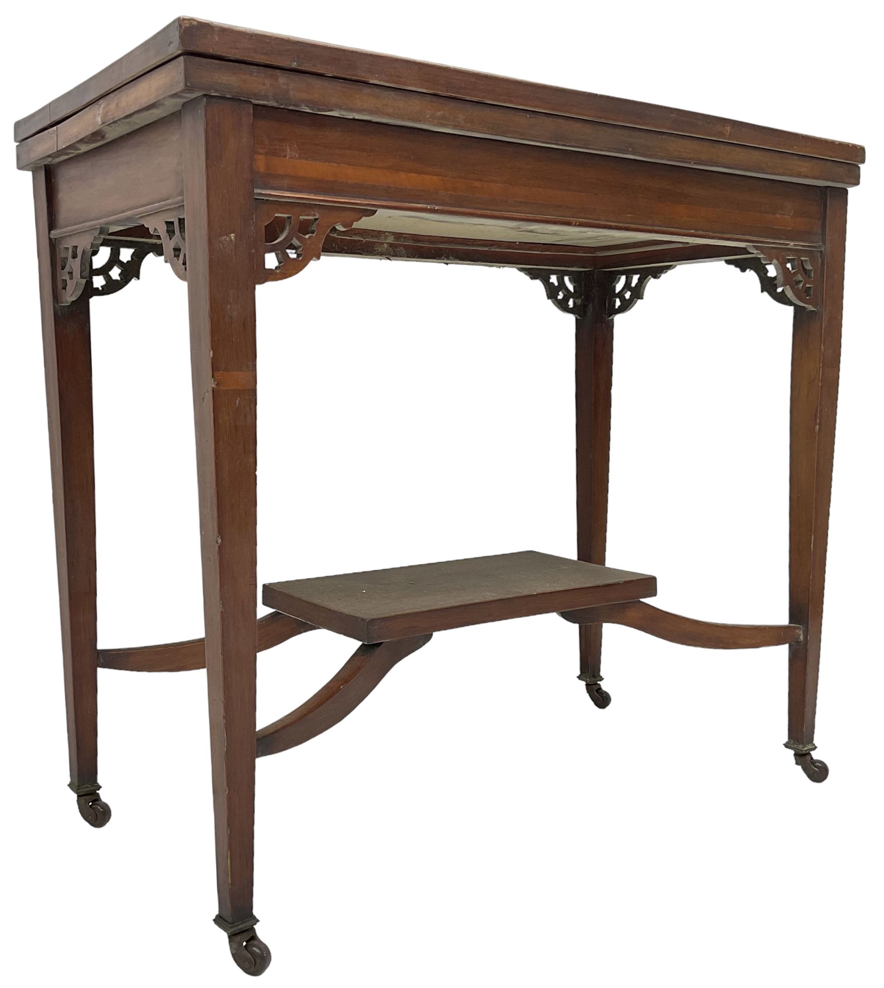 Edwardian inlaid mahogany games table, the rectangular fold-over swivel top decorated with central shell motif inlay and ebony stringing, raised on tapering supports united by shaped X-stretcher and undertier