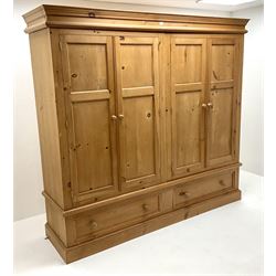 Large solid pine wardrobe, projecting cornice, four doors enclosing hanging rails above two drawers, platform base