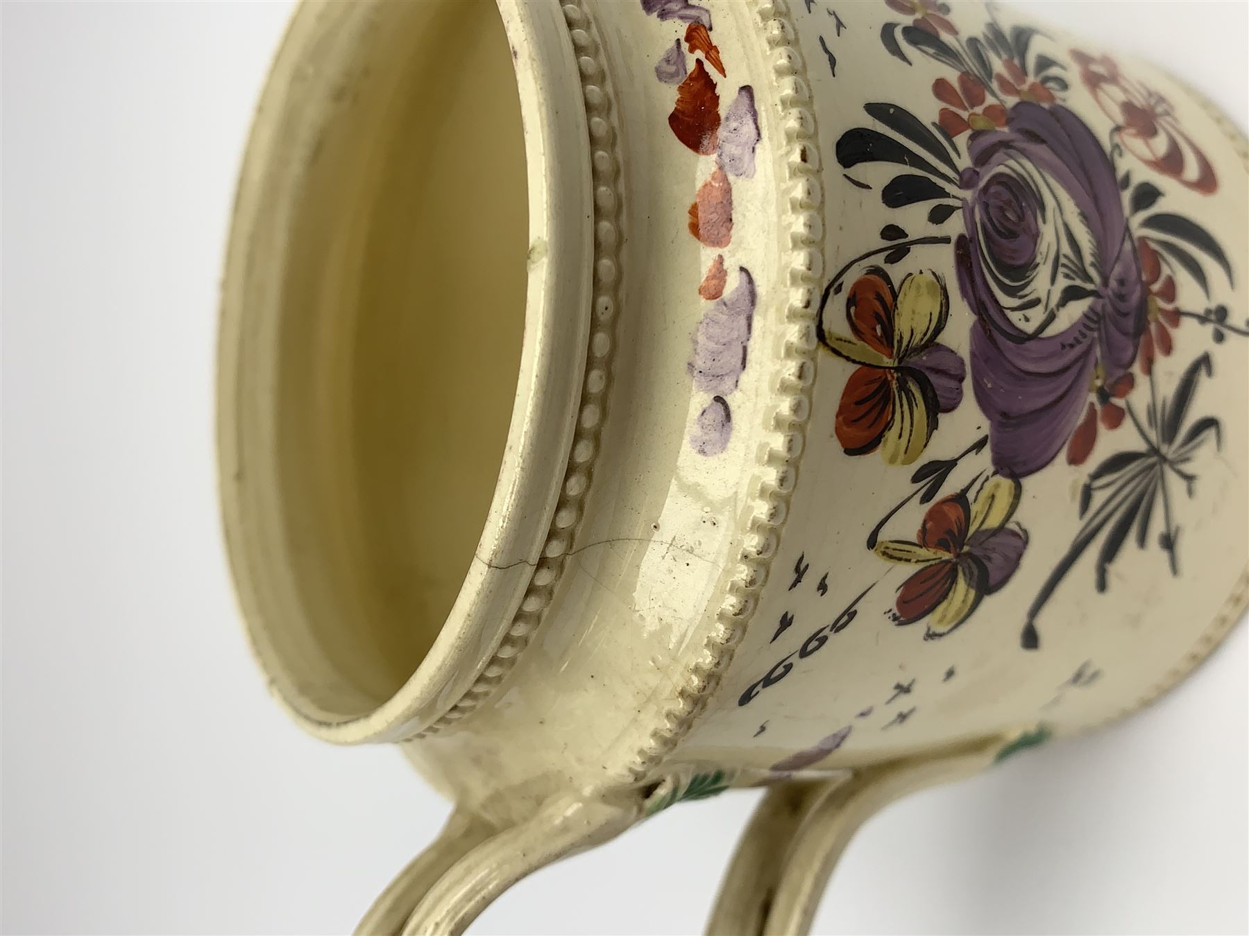 18th century creamware teapot, probably Leeds, with reeded entwined handle and floral finial to the cover, the body with hand painted polychrome decoration of figure to one side, and floral spray to the other, collectors paper label beneath inscribed Leeds Pottery, H11.5cm