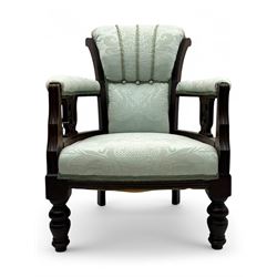 Late Victorian carved mahogany open armchair, the shaped back with fluted upholstered panel and padded arms above pierced scroll carved side supports, over a broad upholstered seat, on turned front supports