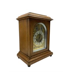 Jungans-German Edwardian 8-day oak cased mantle clock, with a stepped flat top and glazed door on a shallow plinth with bun feet, brass dial with cast spandrels, silvered chapter with Arabic numerals, chime/silent and pendulum regulation dials, three train spring driven movement sounding the quarters on gong rods and the hours on a coiled gong. With pendulum.