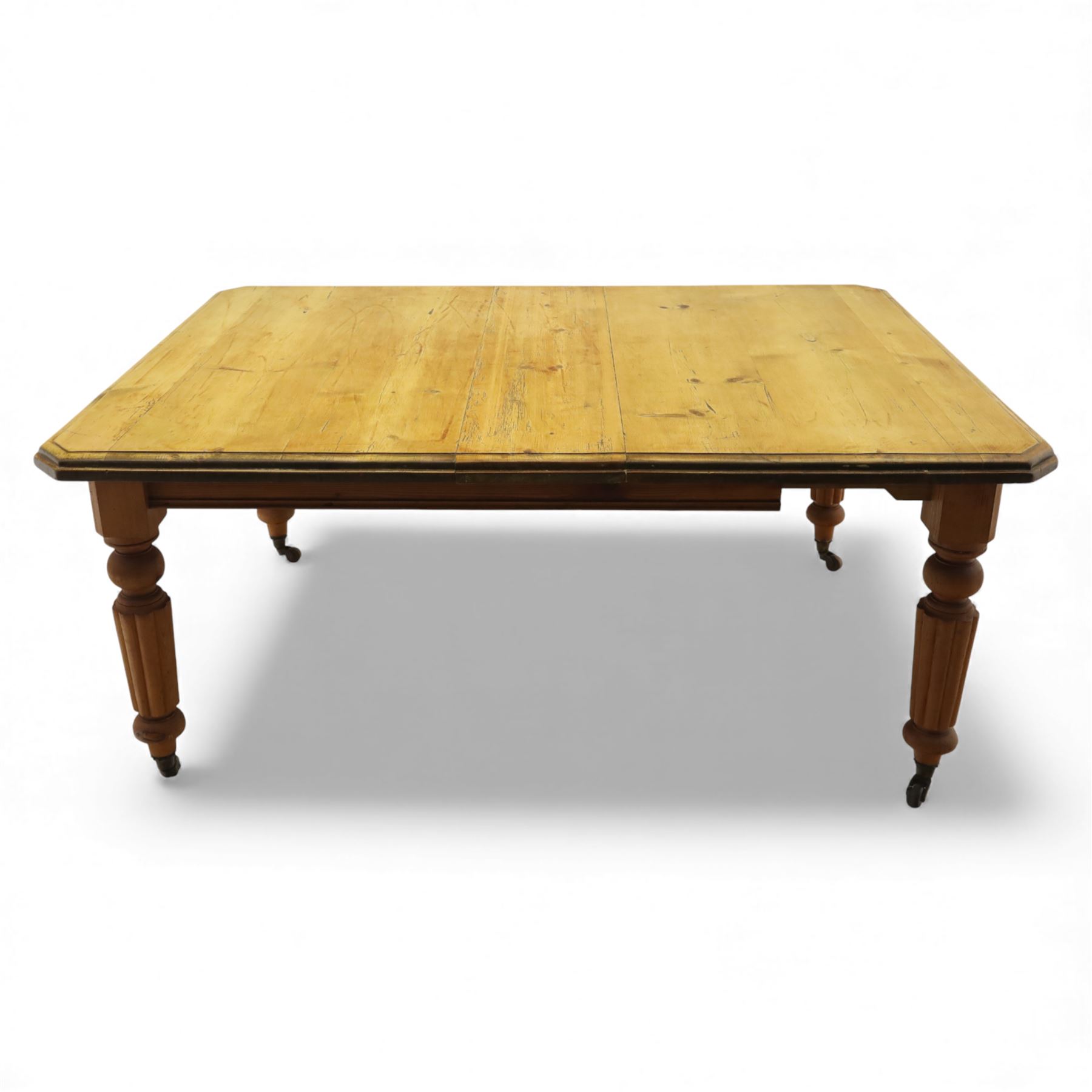 Early 20th century stripped pine kitchen table, the rectangular planked top with moulded edge and canted corners, upon stained pine turned and fluted legs with castors