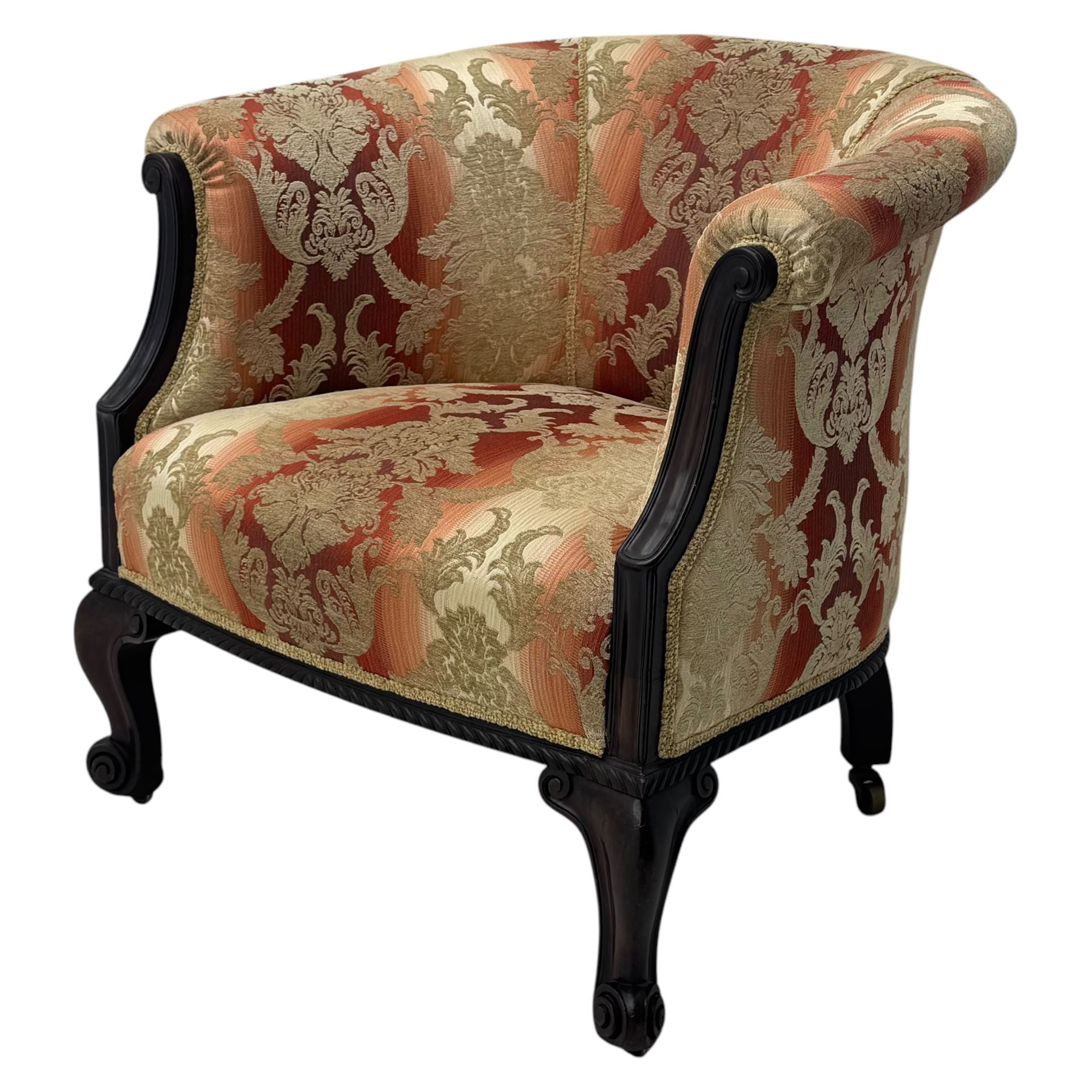 Early 20th century mahogany framed upholstered tub armchair, scrolled arms, upholstered in a damask-style fabric with foliate pattern, raised on cabriole front legs upon brass castors