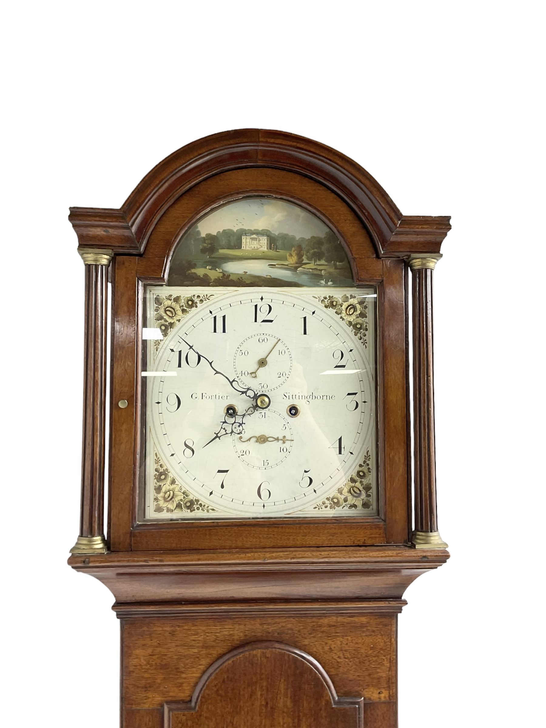 G Fortier of Sittingborn - Early 19th century 8-day mahogany longcase clock c1825, with a break arch pediment and hood door flanked by reeded pilasters with brass capitals, plain case with a long trunk door with a conforming break arch top, plinth with applied skirting, painted dial with upright Arabic numerals, date  and seconds dials, floral spandrels and a rural depiction of a country house and river to the arch, replacement steel hands with brass pointers to the calendar and seconds dials, dial pinned directly to a rack striking movement. With weights, pendulum and winding key.
