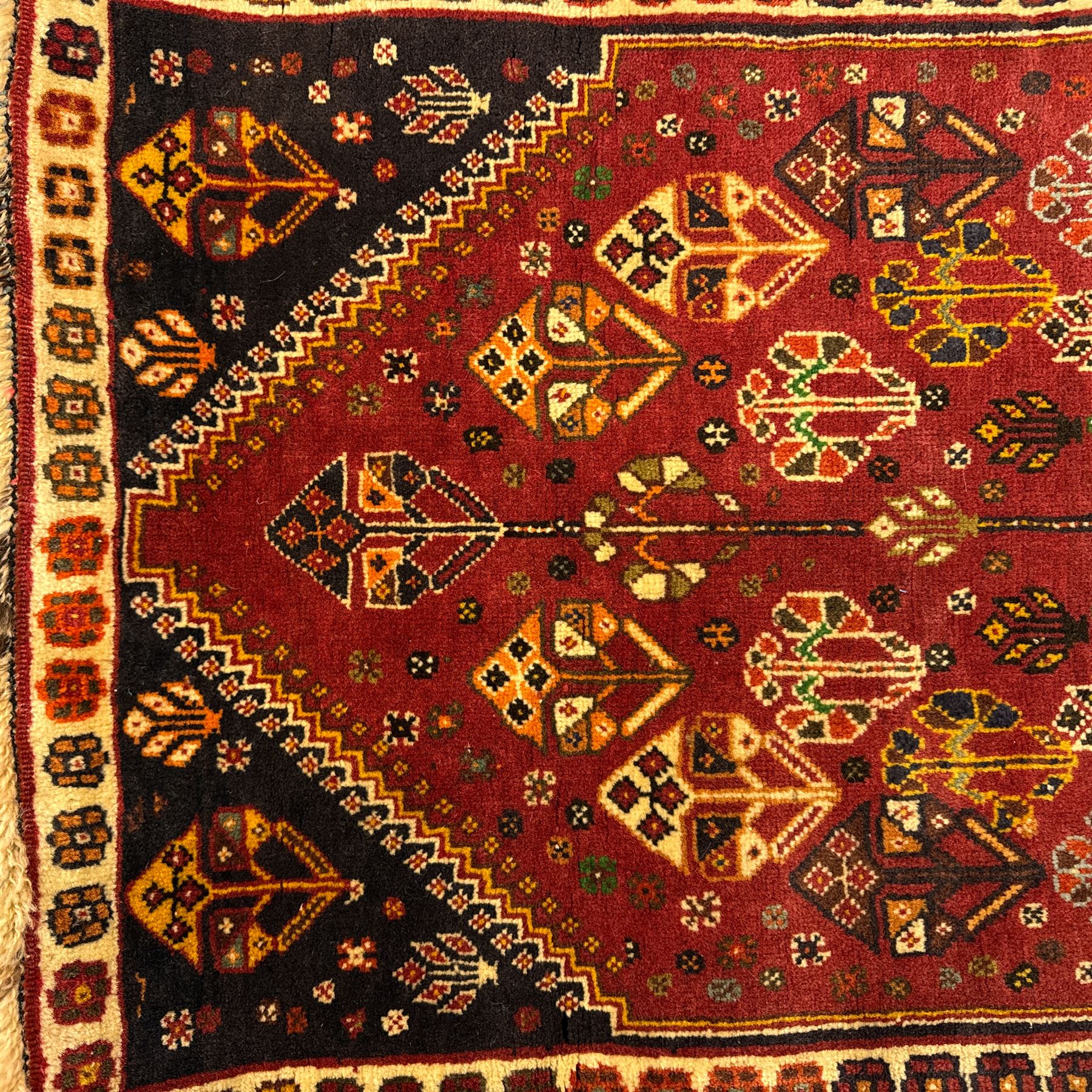 South West Persian Qashqai rug, hand knotted wool with central dark blue lozenge medallion containing geometric motifs, on a madder red field decorated with stylised floral boteh motifs, indigo spandrels, multiple borders of floral rosettes, from the region of Fars, south-west Persia