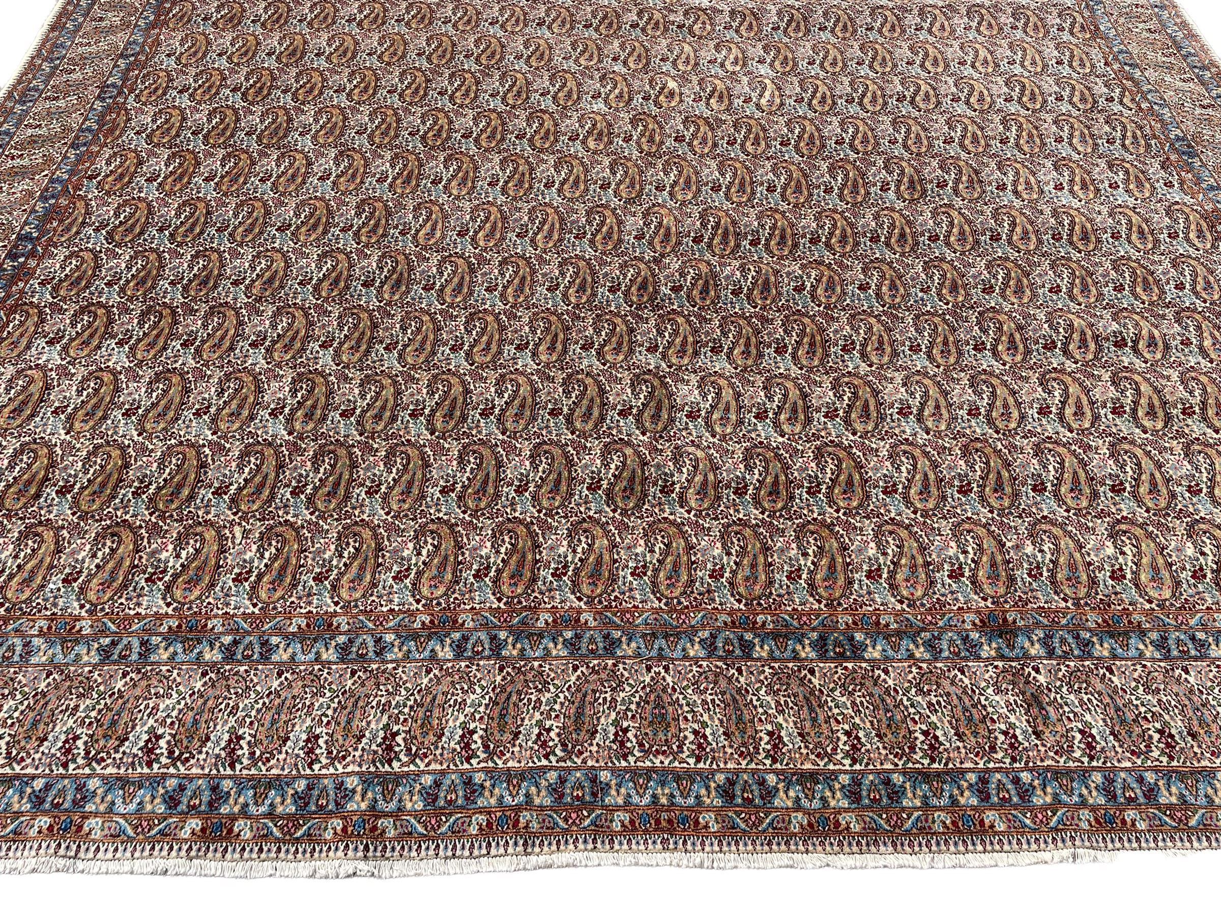 Persian Kirman carpet, the ivory ground field and border decorated with repeating Boteh motifs, interspaced with all-over floral design, blue ground border guards, the top border with signature panel