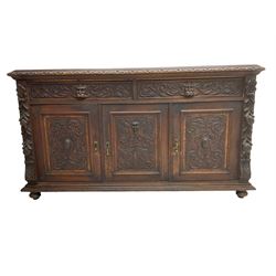 Victorian heavily carved oak sideboard, the moulded top carved with foliate decoration to the edge, fitted with two drawers and three cupboards, the drawer fronts carved with green man mask handles and scrolling foliage, the panelled doors carved with interlacing foliage, on turned compressed bun feet