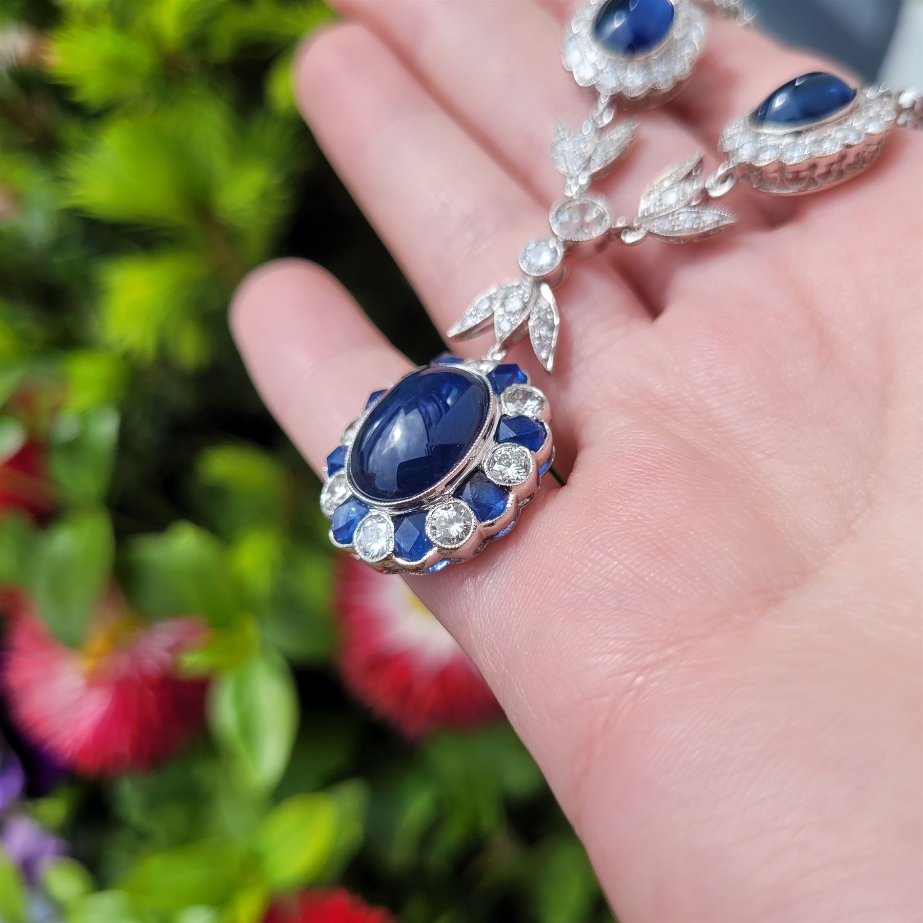 18ct white gold sapphire and diamond milgrain set necklace, oval cabochon cut sapphire surrounded by eight round brilliant cut diamonds and eight French cut sapphires, suspending from a diamond set leaf pendant, single round brilliant cut diamond and a larger old cut diamond, the chain set with six graduating cabochon cut sapphires, each surrounded by diamonds and spaced by a single diamond and a diamond set leaf, to a belcher link chain necklace, hallmarked, total sapphire weight approx 27.00 carat, total diamond weight approx 7.50 carat