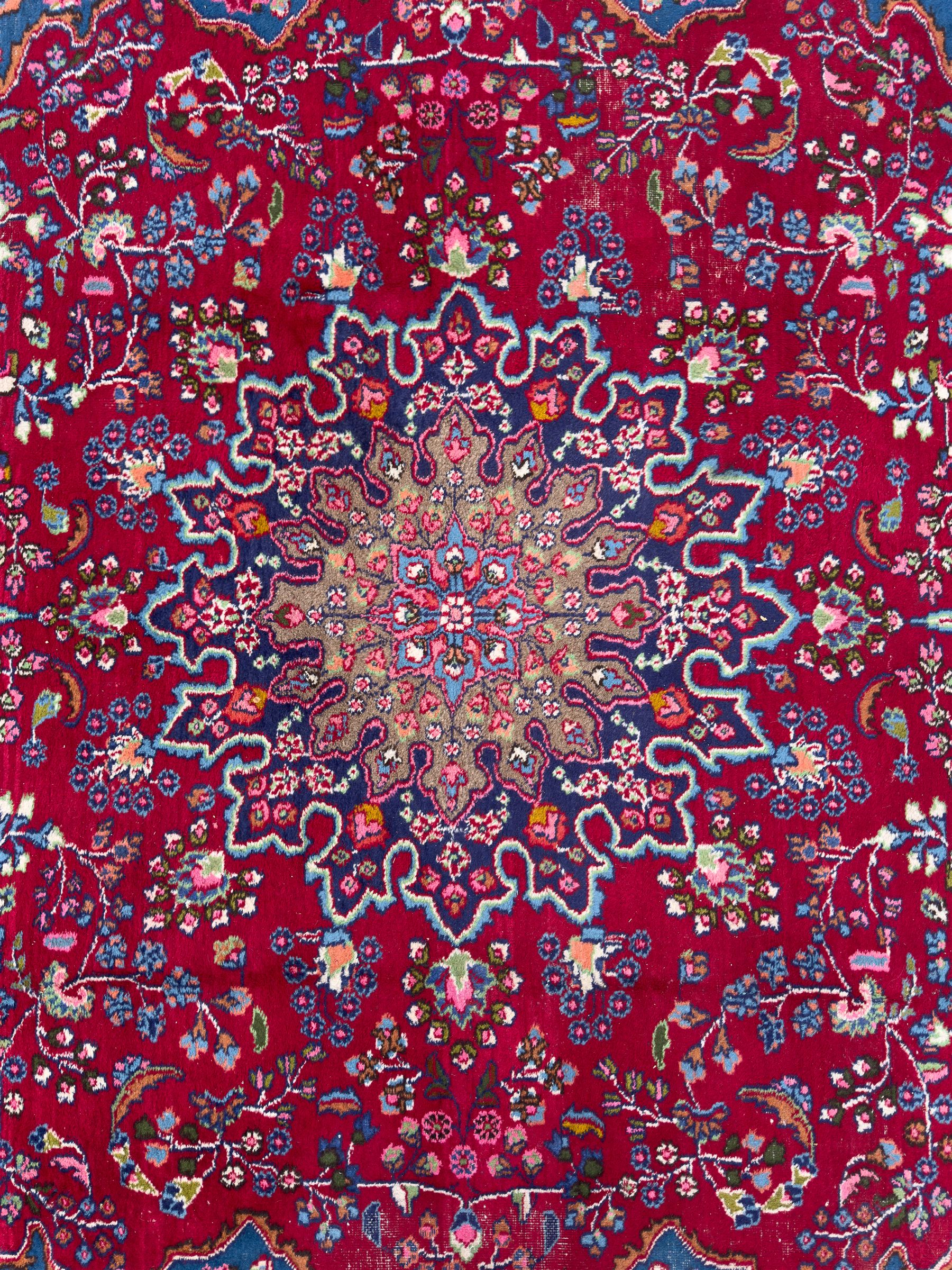 Pair of Persian wool rugs, each with rich red ground, one centred with a diamond-shaped medallion and navy spandrels within a floral field, the other with radiating floral medallion and scrolling foliate motifs, both enclosed by multiple borders with palmette and flowerhead designs, from the region of Kashan 291x376, 299 x 378 