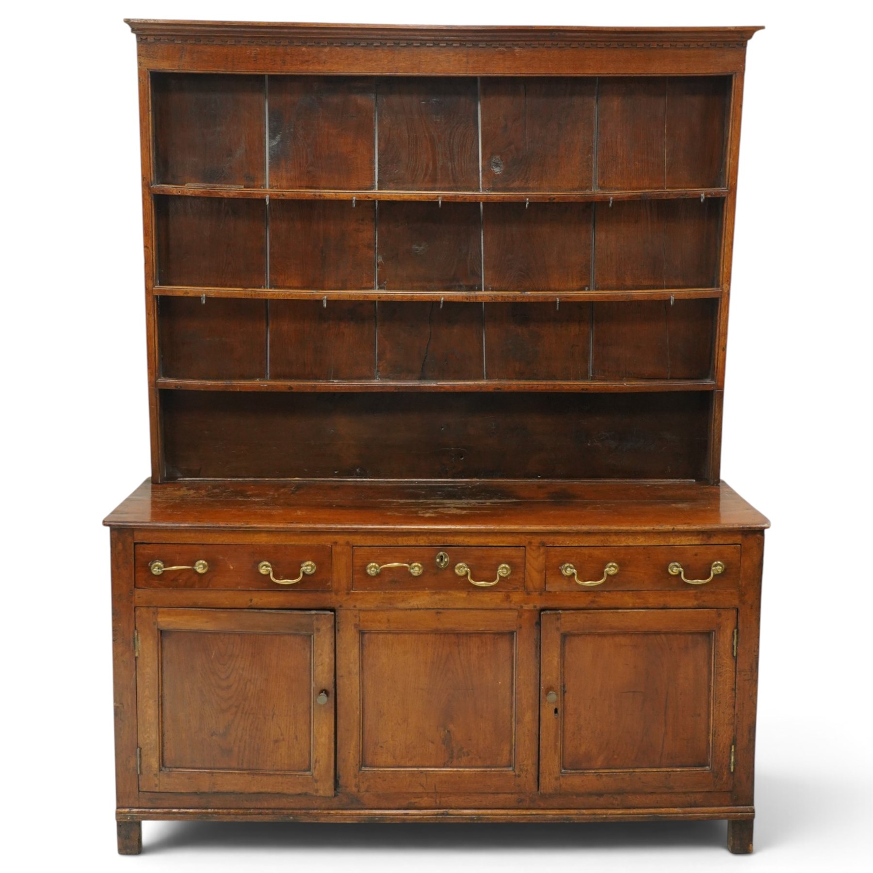 18th century oak dresser with rack, the three-tier plate rack with dentil-carved cornice, the plate shelves with moulded edge and wrought metal hooks, the base fitted with three drawers with brass swan-neck handles over three panelled cupboards, lower moulded edge on stile supports