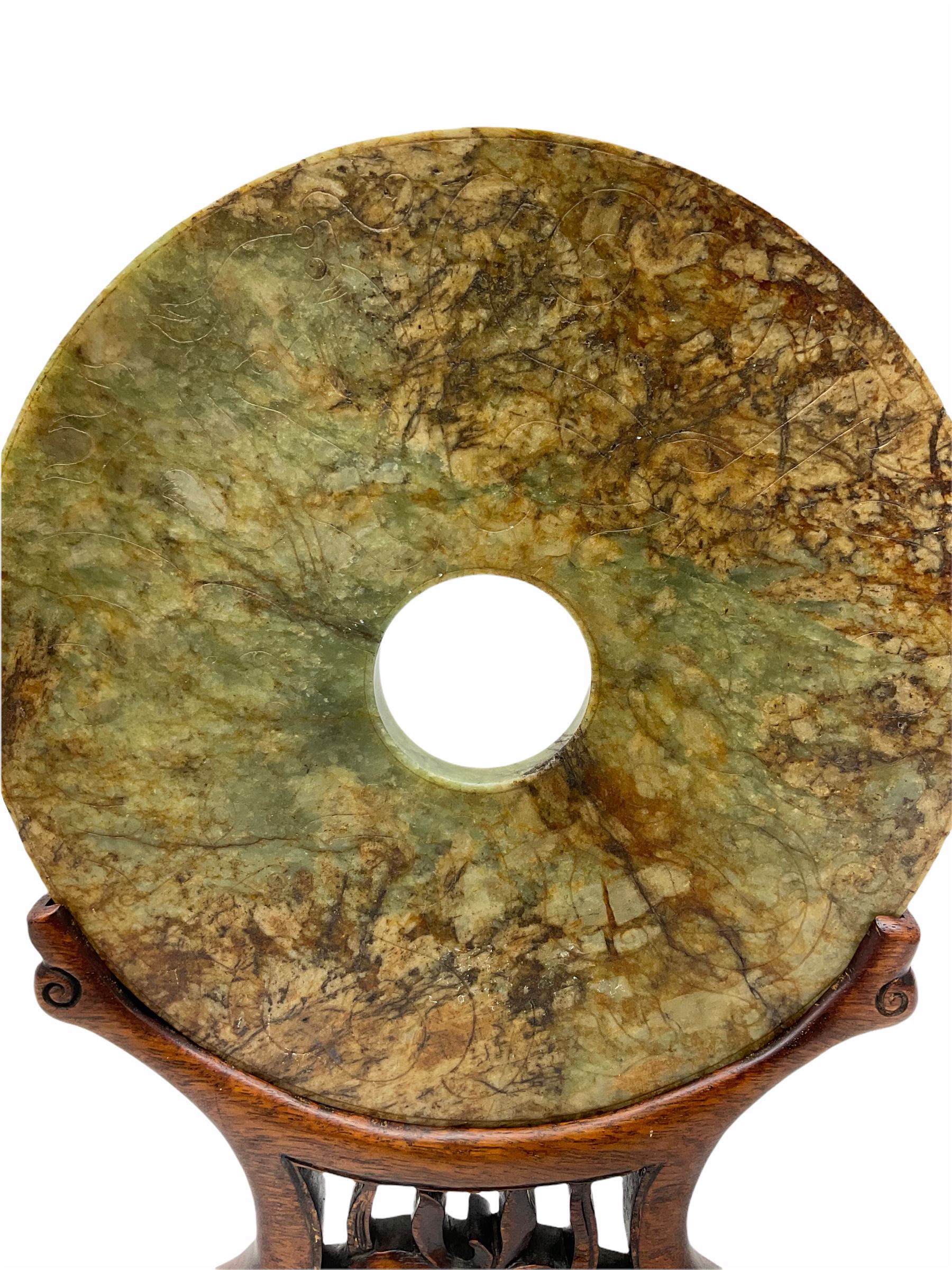 Large Chinese green and russet jade Bi-Disc, engraved with Taotie masks and tigers in the style of the Western Han dynasty, upon carved hardwood stand, disk D21cm