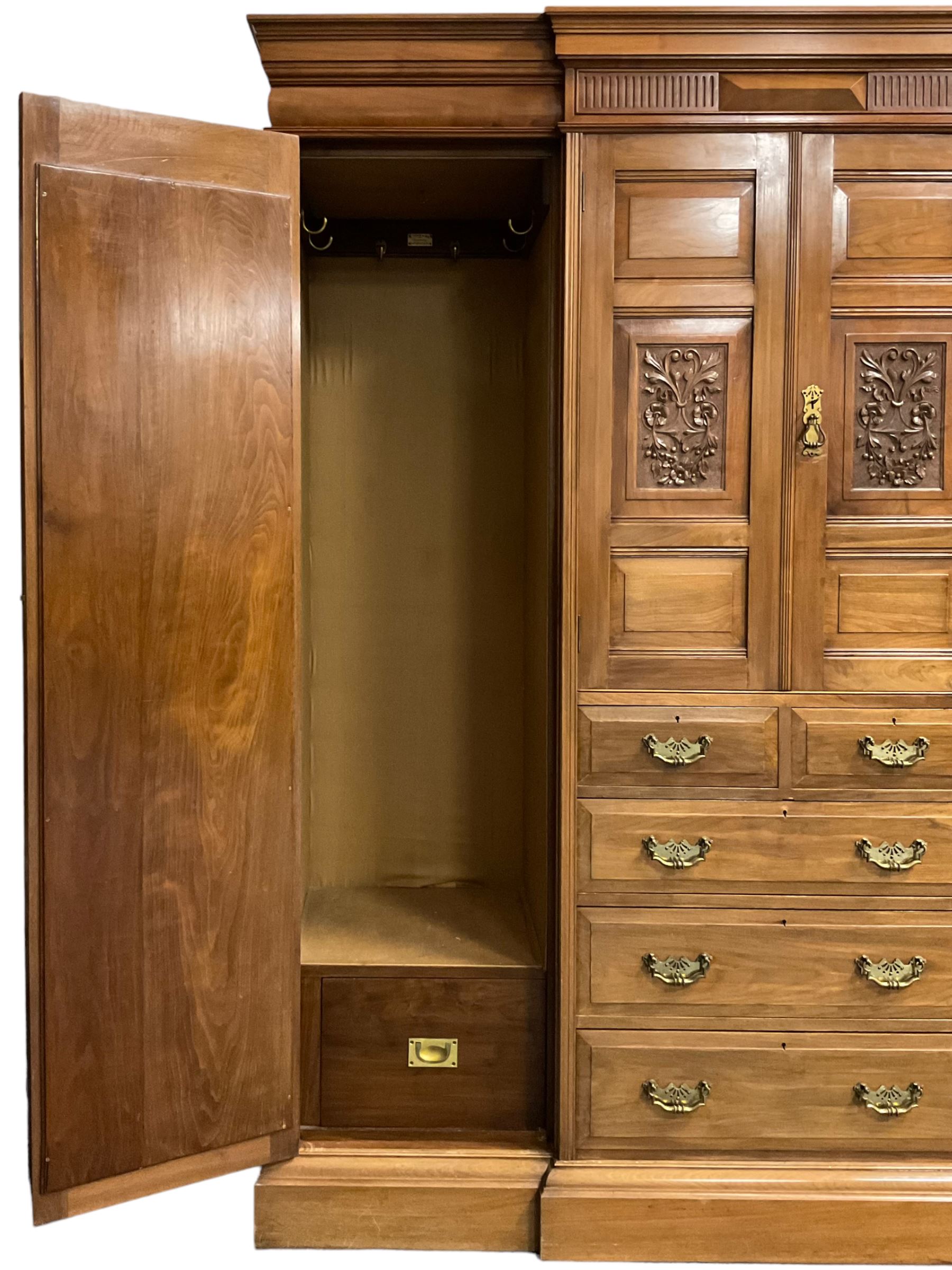 Edwardian walnut combination breakfront triple wardrobe, projecting cornice over cushioned and fluted frieze, central fielded panelled cupboard carved with foliate decoration above two short and three long drawers, flanked by two bevelled mirror doors enclosing hanging hooks with single drawers to base, retailed by J Tonks & Sons, Scarborough