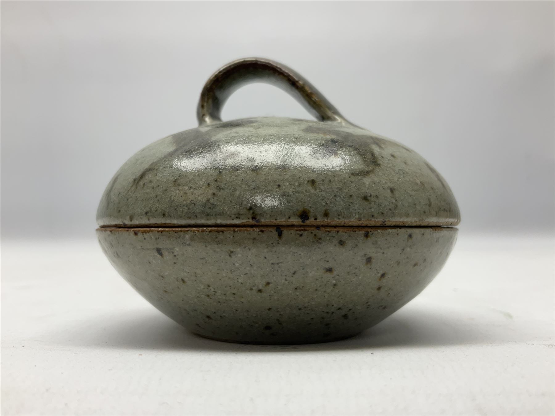 Janet Leach (American, 1918-1997) for Leach Pottery; speckled studio pottery vase of shouldered ovoid form with speckled brown decoration and trailing green and brown glaze upon beige and brown ground, with impressed J.L. monogram and Leach Pottery mark beneath, together with a Jeremy Leach blue speckled lidded circular dish with loop handle, impressed J.L, tallest H11cm