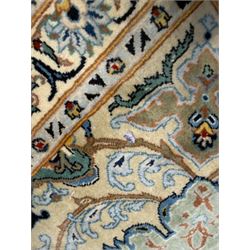 Central Persian Kashan hand-knotted carpet, ivory field with scrolling vines, palmettes, and rosettes around a cusped medallion with pendants and spandrels within a blue ground border of palmettes and flowerheads, 388cm x 300cm