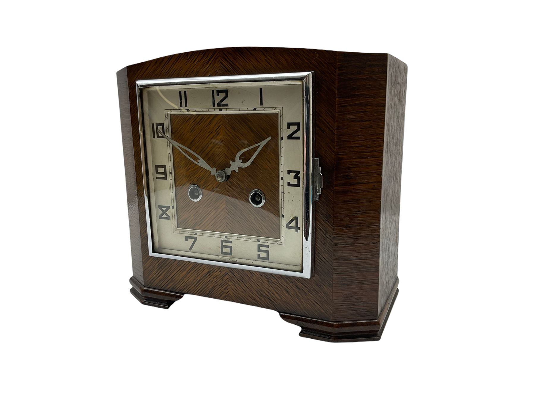 A 1930’S Art Deco 8-day striking mantle clock in a rectangular oak case on raised feet, with a corresponding square dial, hours in Arabic numerals and minute track, with pierced silvered hands, chrome winding collets and a square chrome bezel, striking the hours and half-hours on a coiled gong. 
With pendulum.

