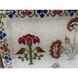 Victorian wool work sampler, depicting a vignette of a young girl feeding birds, flanked by two houses, and surrounded by urns of flowers and flowering plants, within a fruiting vine border, in maple frame, overall H47.5cm W49.5cm