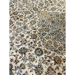 Central Persian Kashan pale khaki ground carpet, shaped central medallion enclosing small stylised motifs, the field decorated profusely with trailing foliate branches and plant motifs, guarded border with repeating floral design 