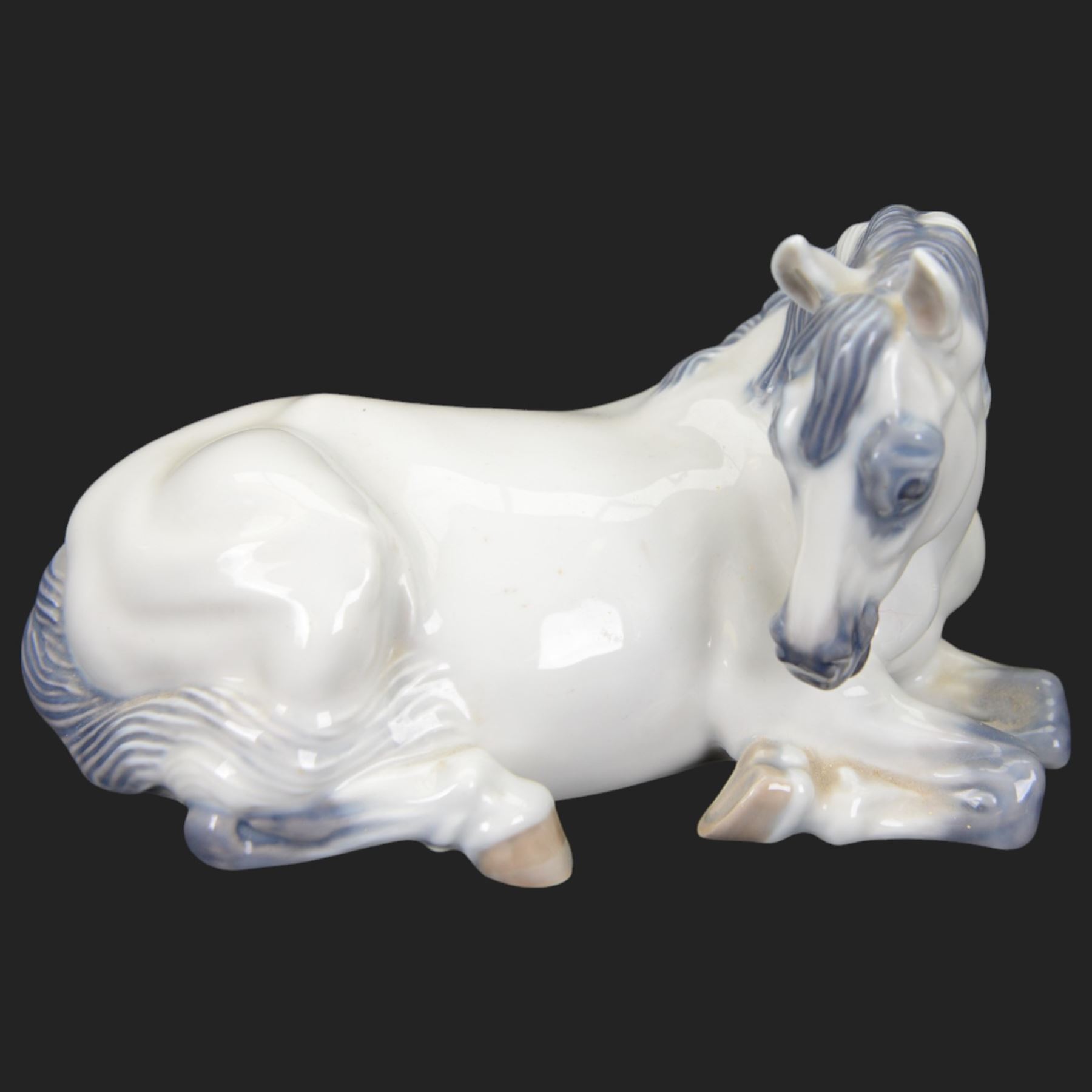 Two Royal Copenhagen figures modelled as Lippizaner horses, the first example in a recumbent pose no 5690, the second example prancing upon a stepped circular base, H19cm 