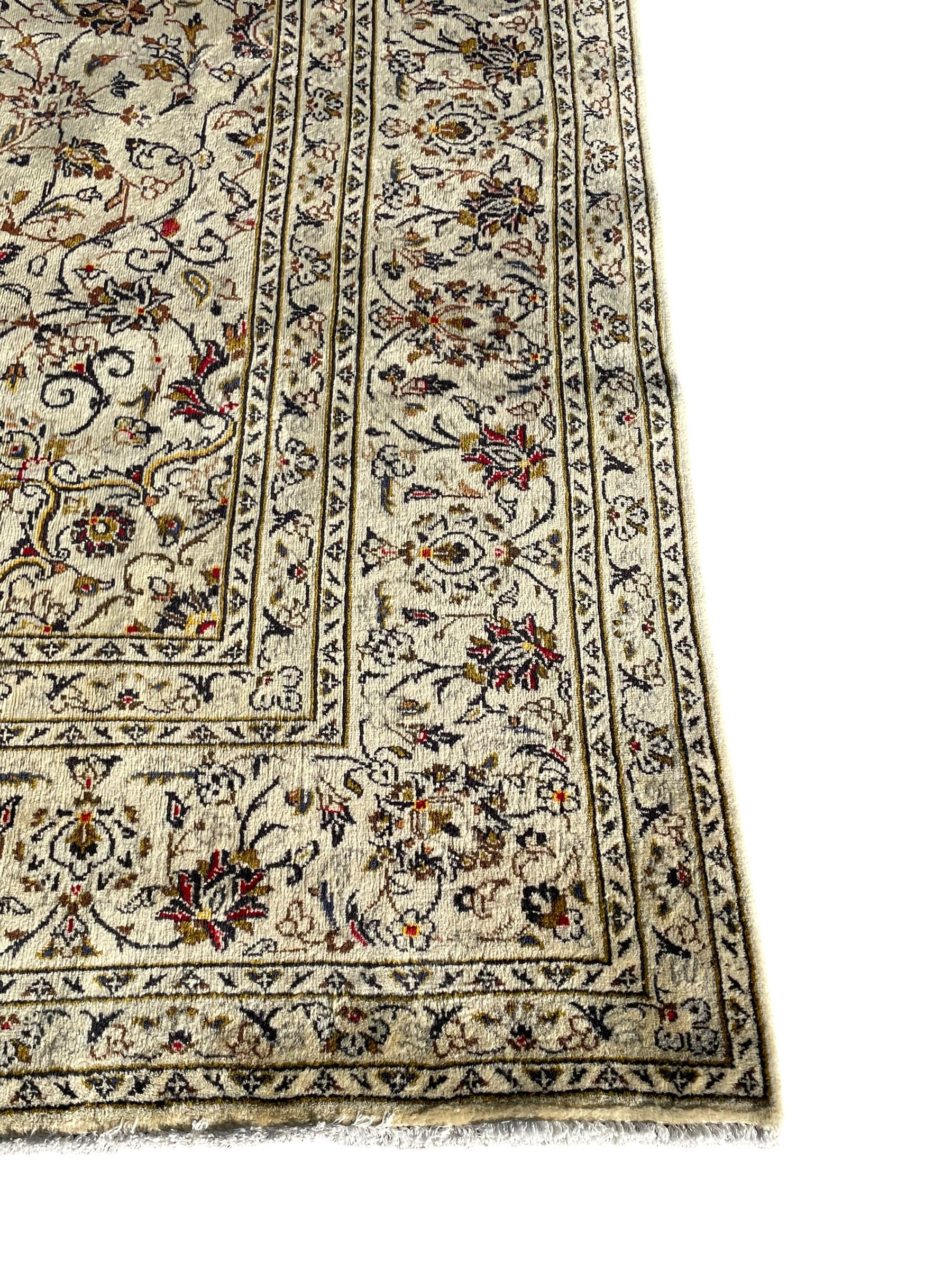 Persian Kashan ivory ground carpet, central medallion decorated with sixteen arranged palmette motifs, within a field decorated with swirling leafy branches and stylised plant motifs, the main border decorated with matching swirling pattern, within floral pattern guard stripes 