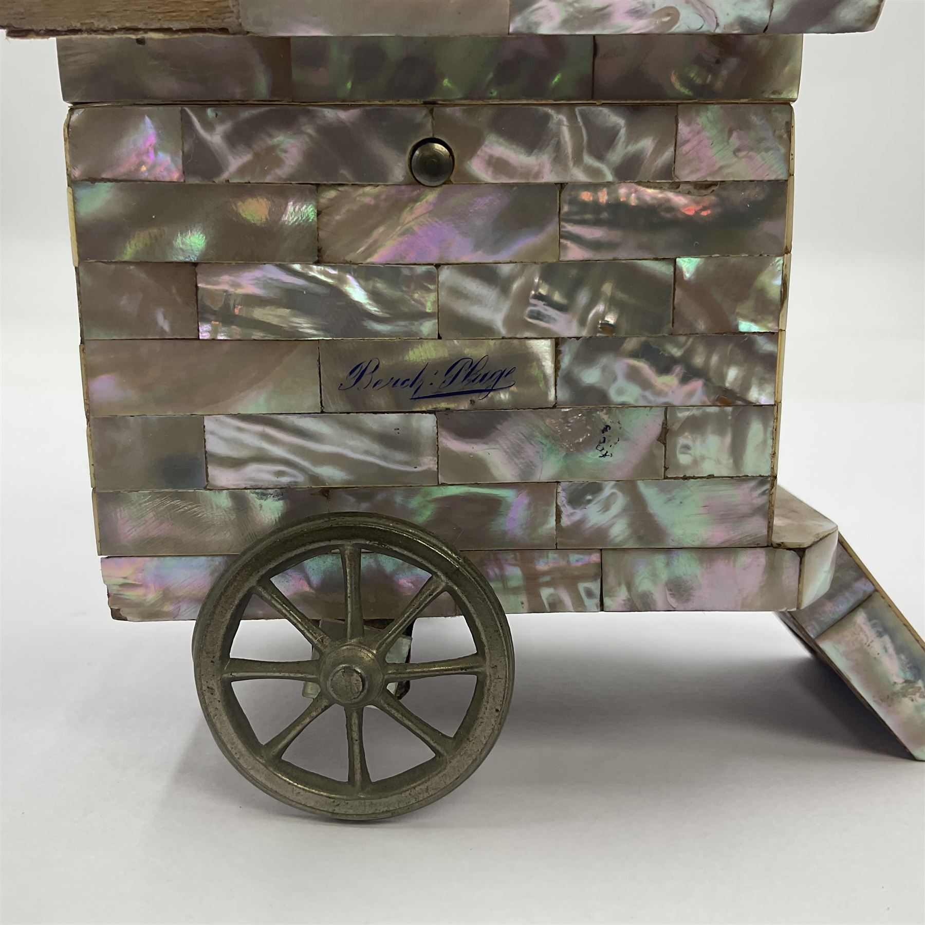 19th century French souvenir jewellery casket in the form of a bathing machine, having mother of pearl panelled tiled effect body, hinged roof/cover revealing a blue silk fitted interior with cushioned base, two silvered metal wheels, abalone shell door and mother of pearl steps, inscribed 'Berck Plage' in blue, H12cm, W13cm 