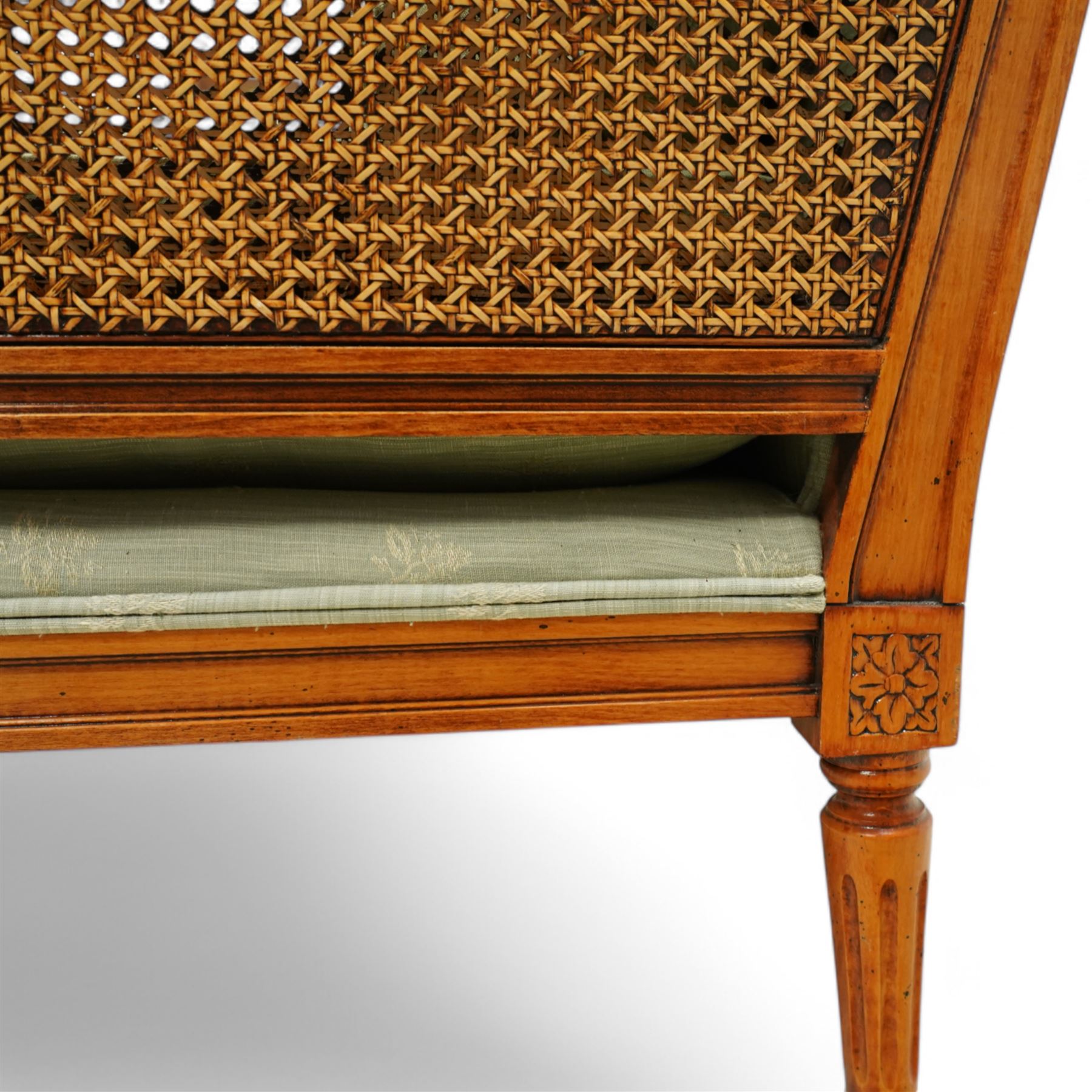 French Empire design varnished wood three piece lounge suite comprising of two cane armchairs and matching sofa, carved top rails with foliate terminals, cane side panels and padded scroll arms, upholstered in a green brocade with matching piping, on fluted legs