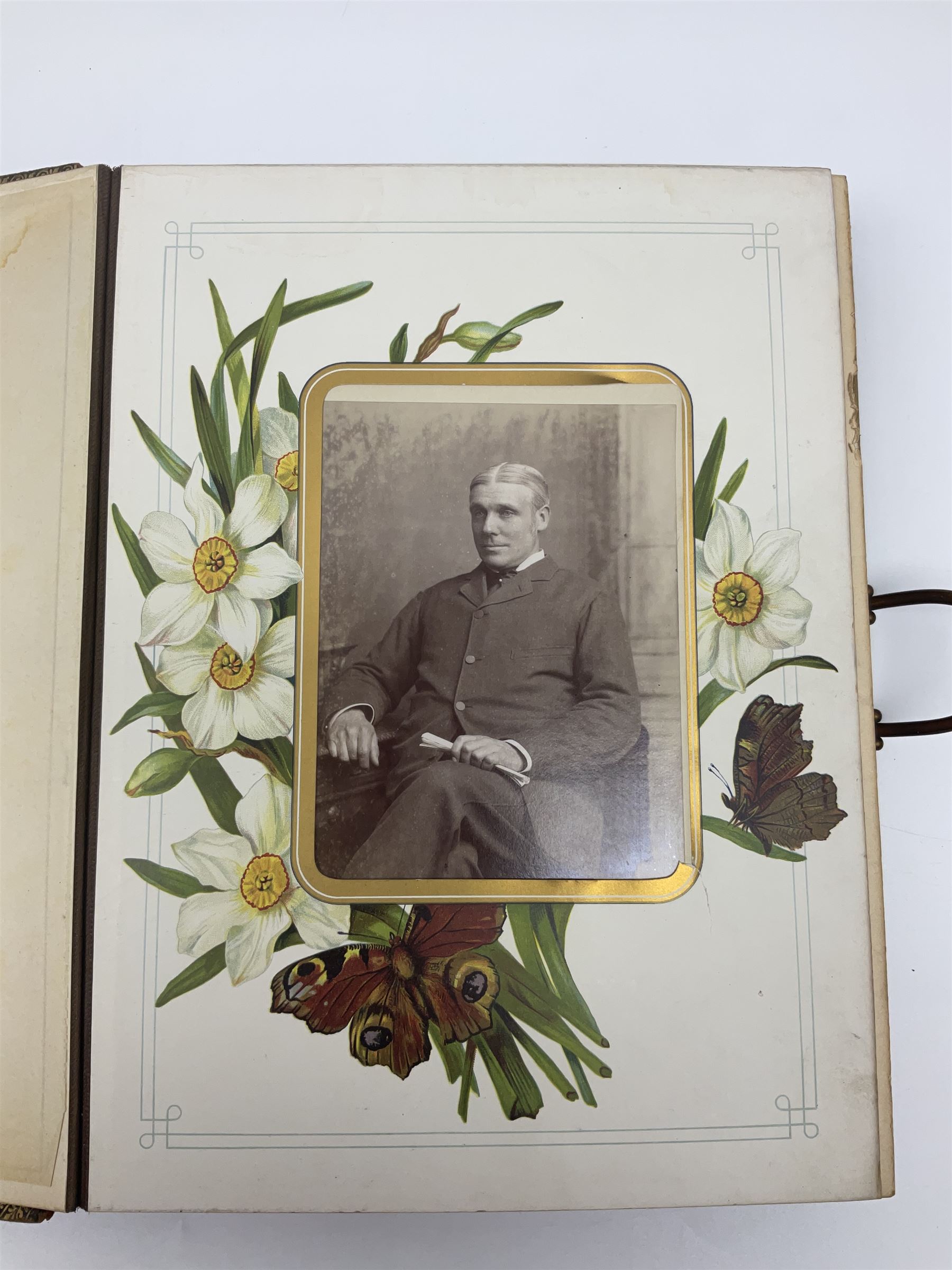  Victorian leather bound photo album, the interior leaves containing apertures of various sizes and shapes of portraits surrounded by printed floral designs, with brass clasp and painted gold decoration to edges, H30cm