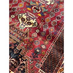 Persian Shiraz red ground rug, the field decorated with various motifs, urns, flower heads and tree of life motifs, enclosed by rectangular bands with geometric decoration, floral repeating border