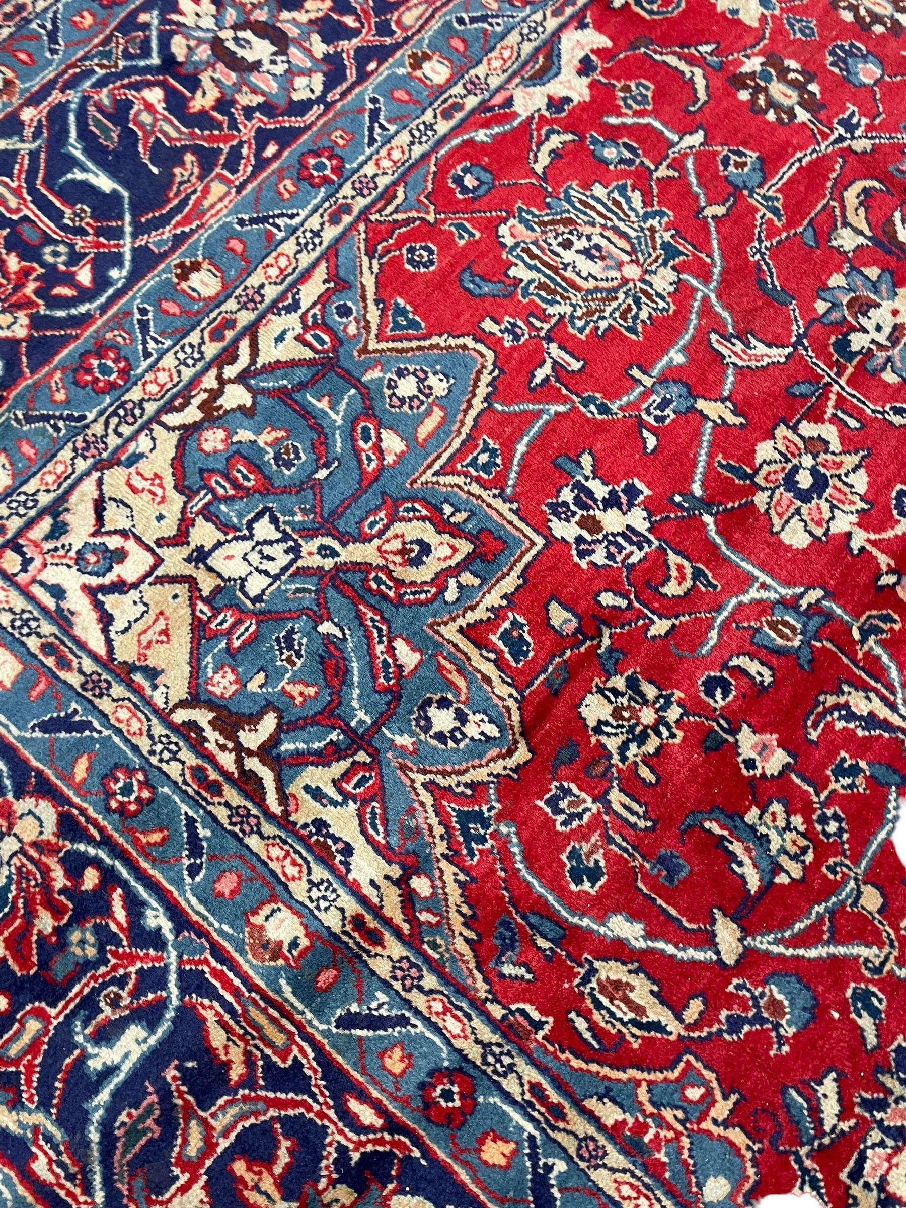 Kashan crimson ground carpet, overall floral design, the central medallion surrounded by trailing leafy branches and palmettes, scrolling border decorated with stylised plant motifs, within guard stripes
