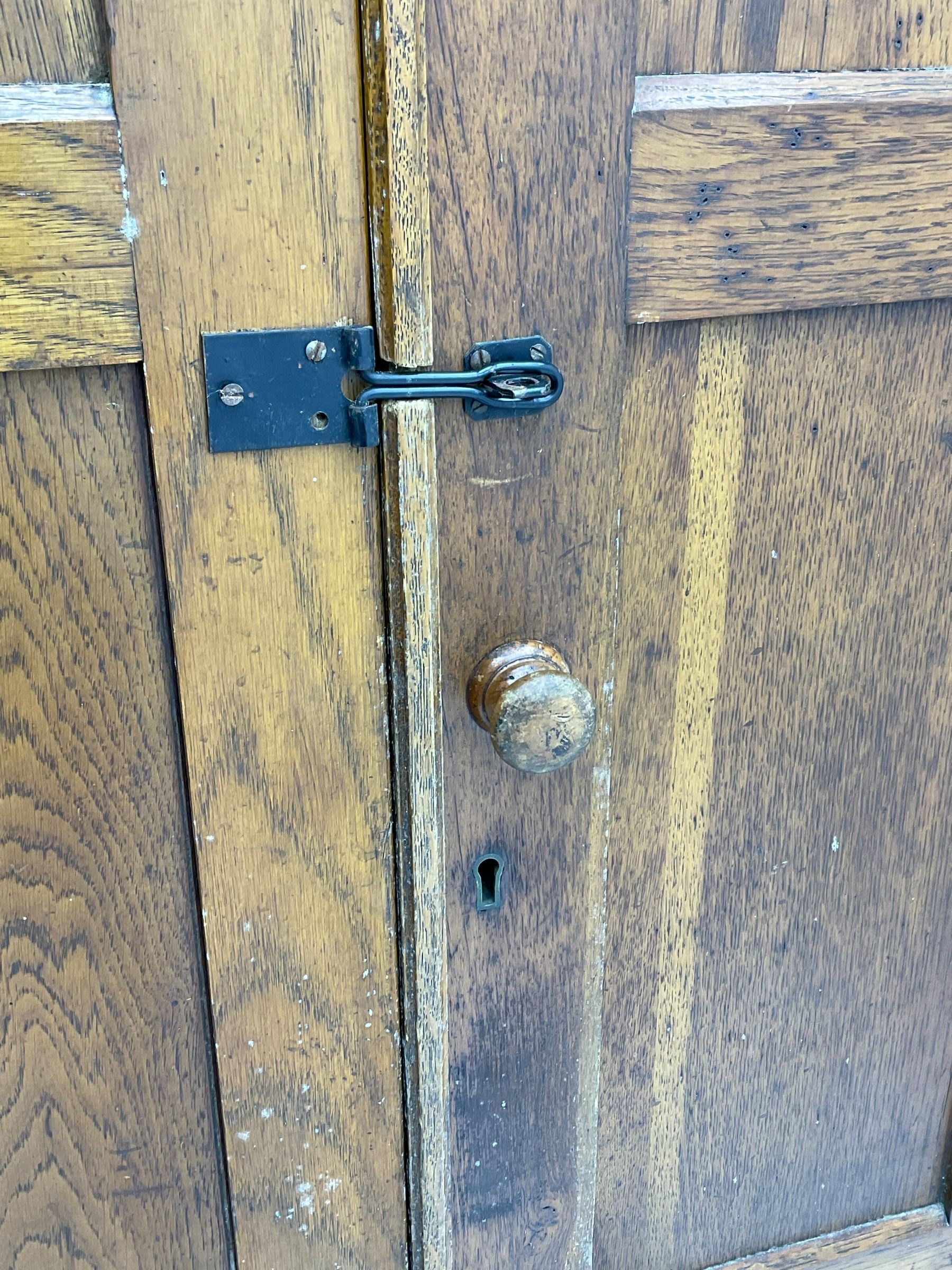 The North of England School Furnishing Company Limited Darlington - early 20th century oak school cupboard, projecting moulded cornice over two panelled doors, fitted with shelves, on chamfered plinth base 