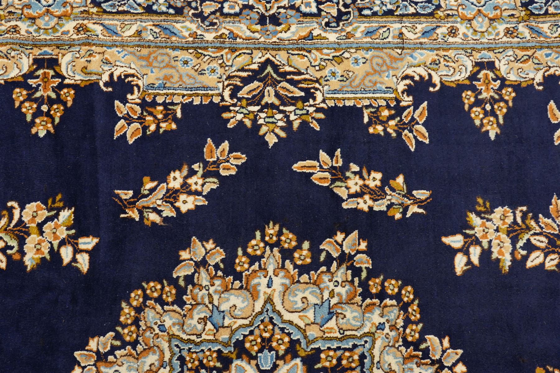South East Persian Kirman hand-knotted carpet, indigo blue field with central floral medallion in tones of ivory, indigo,  and soft blue, issuing network of scrolling vinery, palmettes and floral sprays, conforming spandrels, broad main border of scrolling foliage and stylized palmettes, framed by multiple guard borders, with cotton fringe ends 
