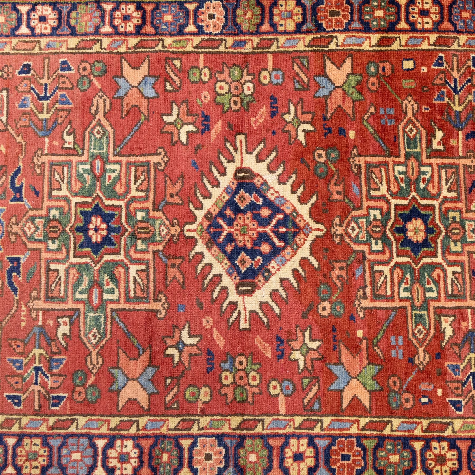 North West Persian Karajeh hand-knotted runner, madder red field, decorated with a vertical sequence of bold geometric medallions, interspersed with stylized floral and tribal motifs, framed by a dark ground border of angular palmettes and rosettes with multiple guard stripes, with cotton fringe ends 