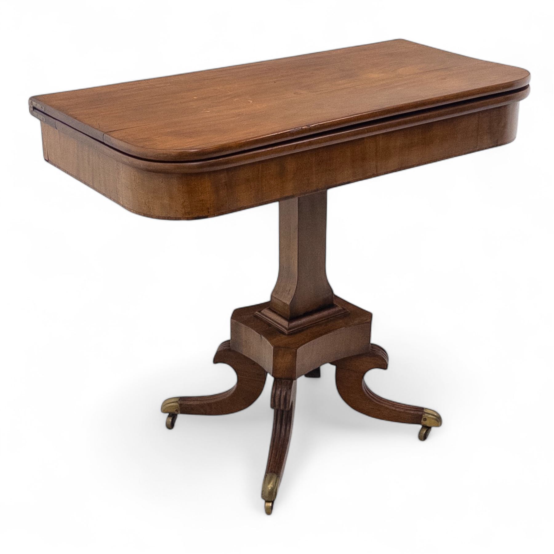 Regency mahogany fold-over table, hinged top with rounded corners opening to reveal a plain polished surface, supported on moulded pedestal base with reeded downswept legs, terminating in brass cups and castors (Extends to 90cm)