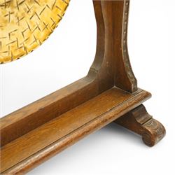Late Victorian Arts & Crafts carved oak framed floor standing dinner gong, the cresting rail carved with central urn and trailing foliage, over shaped end supports decorated with graduating tulip and floral motifs, on rectangular base with scroll sledge feet, the brass gong stamped with William Suckling of Birmingham 'Burmese' makers mark, with striker