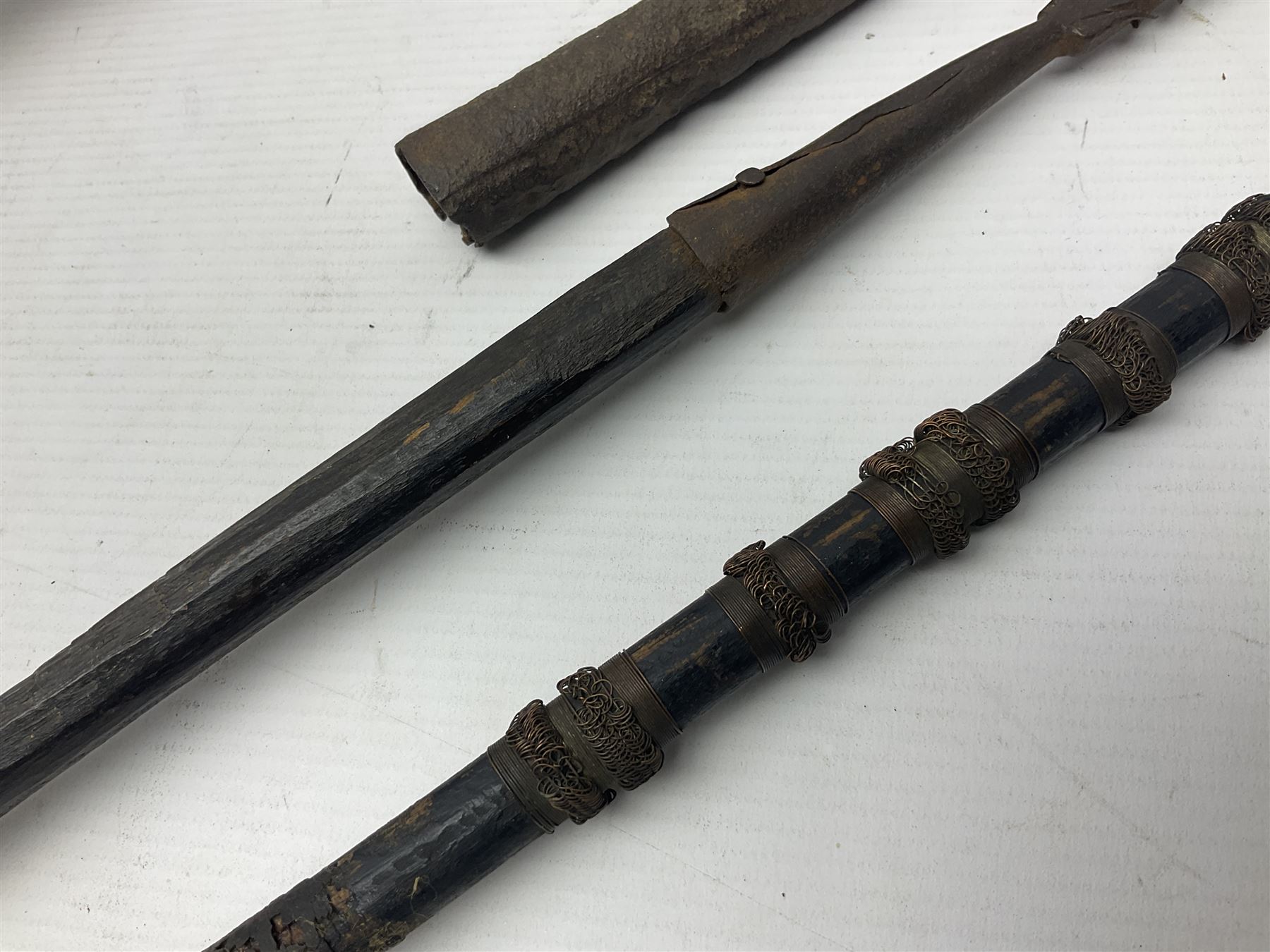 Native hand forged iron fishing spear, the V-shaped head with barbed neck and hewn haft L171cm; and two other hand forged iron spear heads, one with remains of copper bound haft (3)