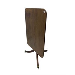 Regency mahogany tilt-top salon table, rectangular top with rounded corners, raised on turned pedestal with splayed tripod base and brass cups and castors