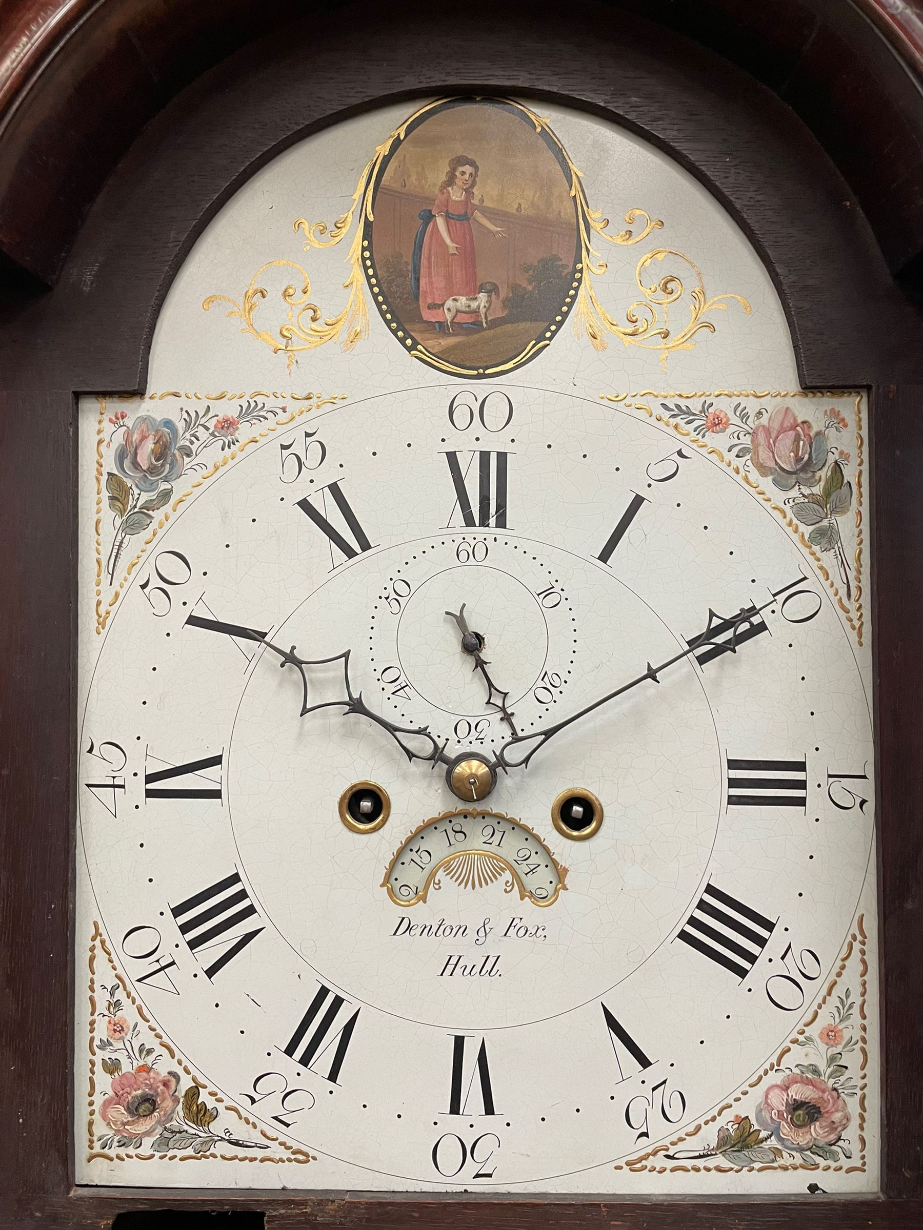 Denton & Fox of Hull – Early 19th century mahogany 8-day longcase clock c1802, pagoda pediment with an oval inlay and three ball and spire finials, break arch painted dial and hood door flanked by reeded pilasters with brass Corinthian capitals, long trunk door with conforming break arch top on a rectangular plinth raised on bracket feet, early Wilson (Birmingham) dial with Roman numerals, five minute Arabic’s and minute dots, subsidiary seconds dial and calendar aperture, with matching steel hands, floral spandrels within raised gesso work and a conforming oval depiction of a young maiden and dog to the break arch, dial pinned via a falseplate to a rack striking movement with a recoil anchor escapement striking the hours on a cast bell. With pendulum and weights.
Joseph Denton was a respected and prolific Hull clock maker working in Scale Lane Hull 1779 and Silver Street 1782-1814. Entering a short-lived partnership with Charles Fox from Beverley in 1802.
