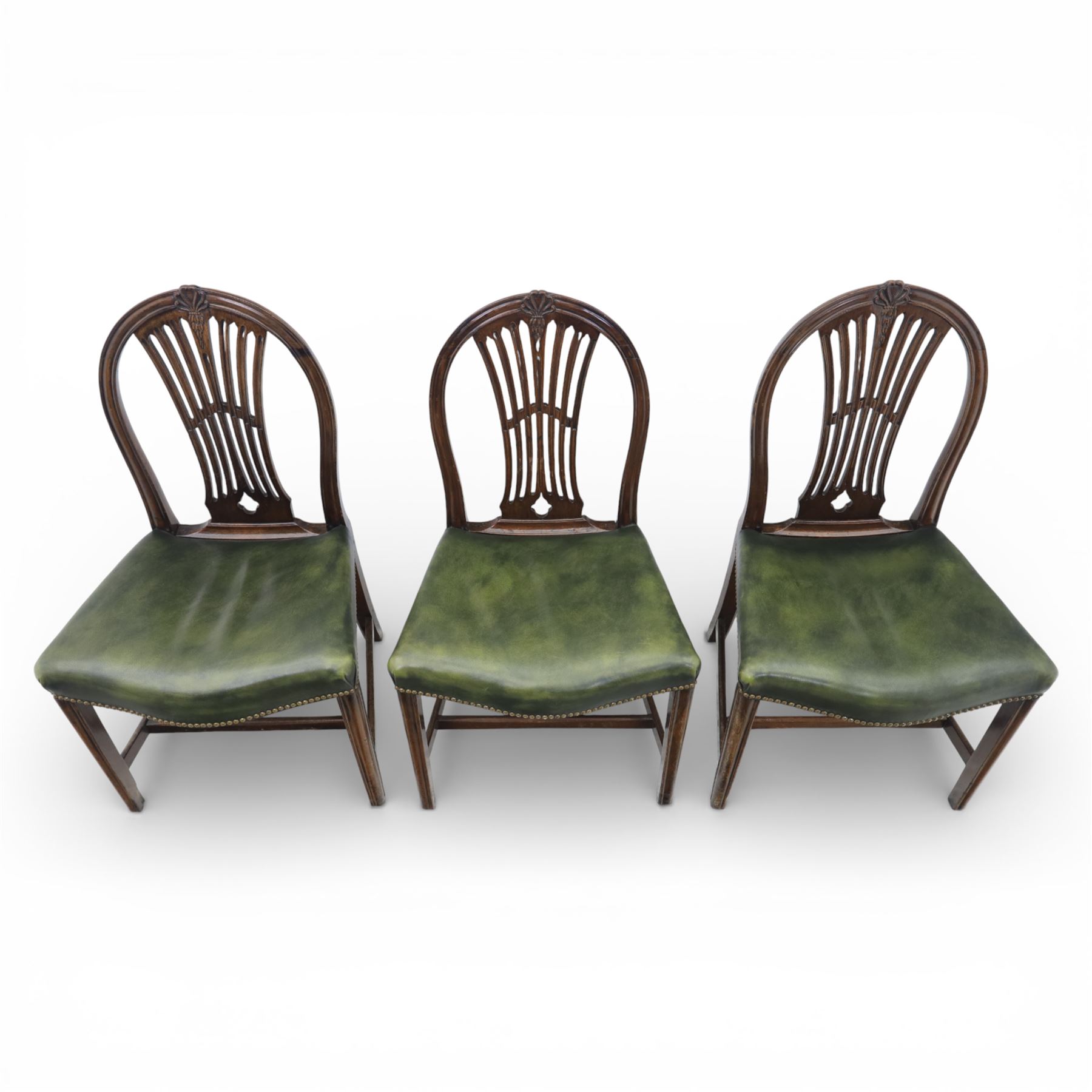 George III style set of six mahogany dining chairs, the arched backs with pierced and carved vase splats beneath carved husk and patera detail, drop-in upholstered seats covered in green leather with brass studded edging, raised on square section legs united by plain stretchers