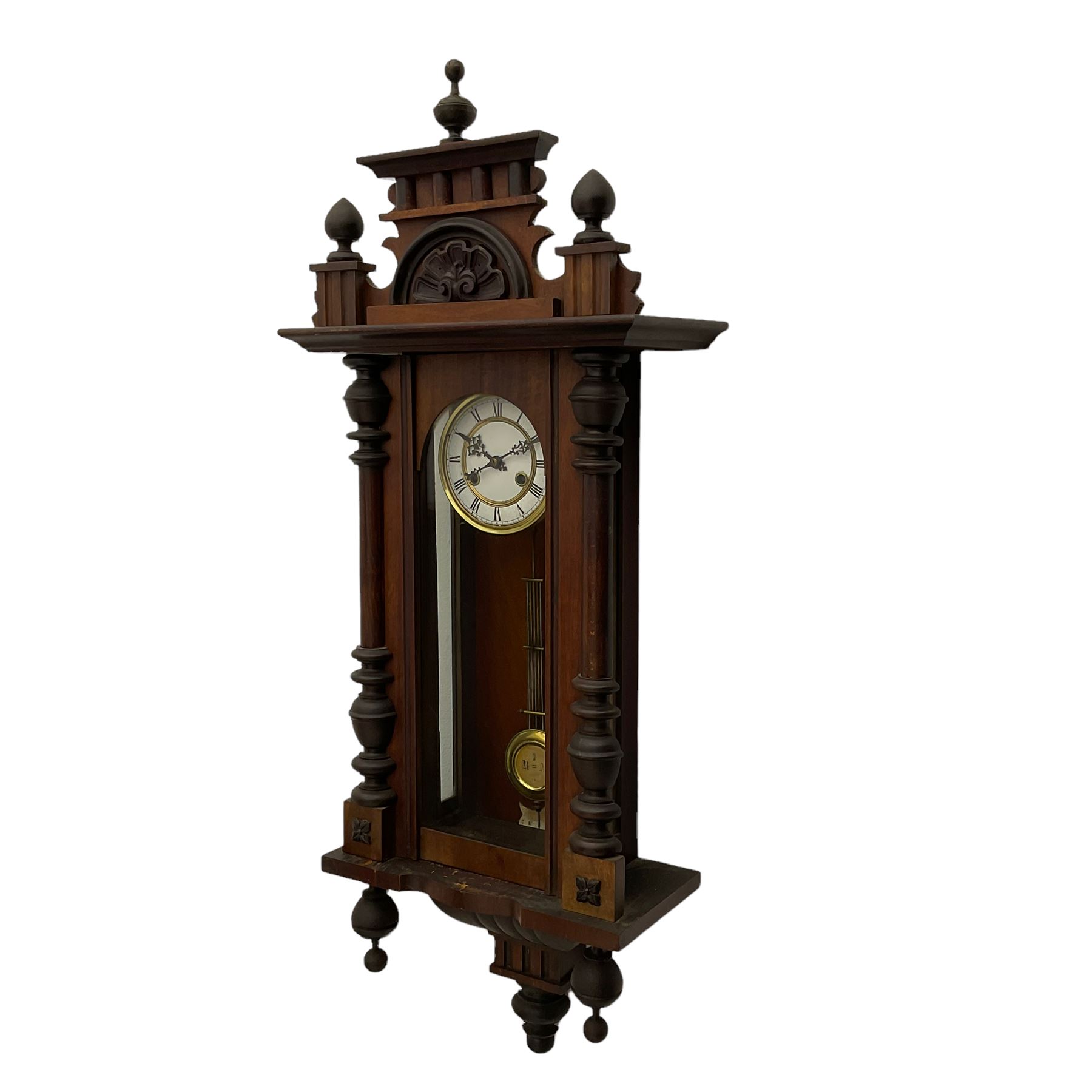 A late 19th century German wall clock with an 8-day spring driven movement striking the hours on a coiled gong, in a mahogany case with a shaped pediment and turned columns flanking a full-length glazed door, with a two-part dial enamel with Roman numerals, minute track and pierced gothic designed hands, gridiron pendulum and beat plate. With Key.




