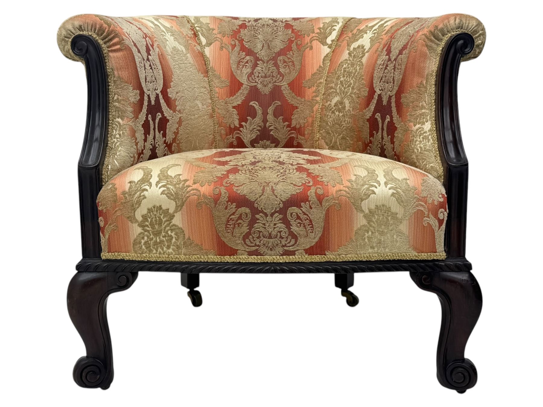 Early 20th century mahogany framed upholstered tub armchair, scrolled arms, upholstered in a damask-style fabric with foliate pattern, raised on cabriole front legs upon brass castors