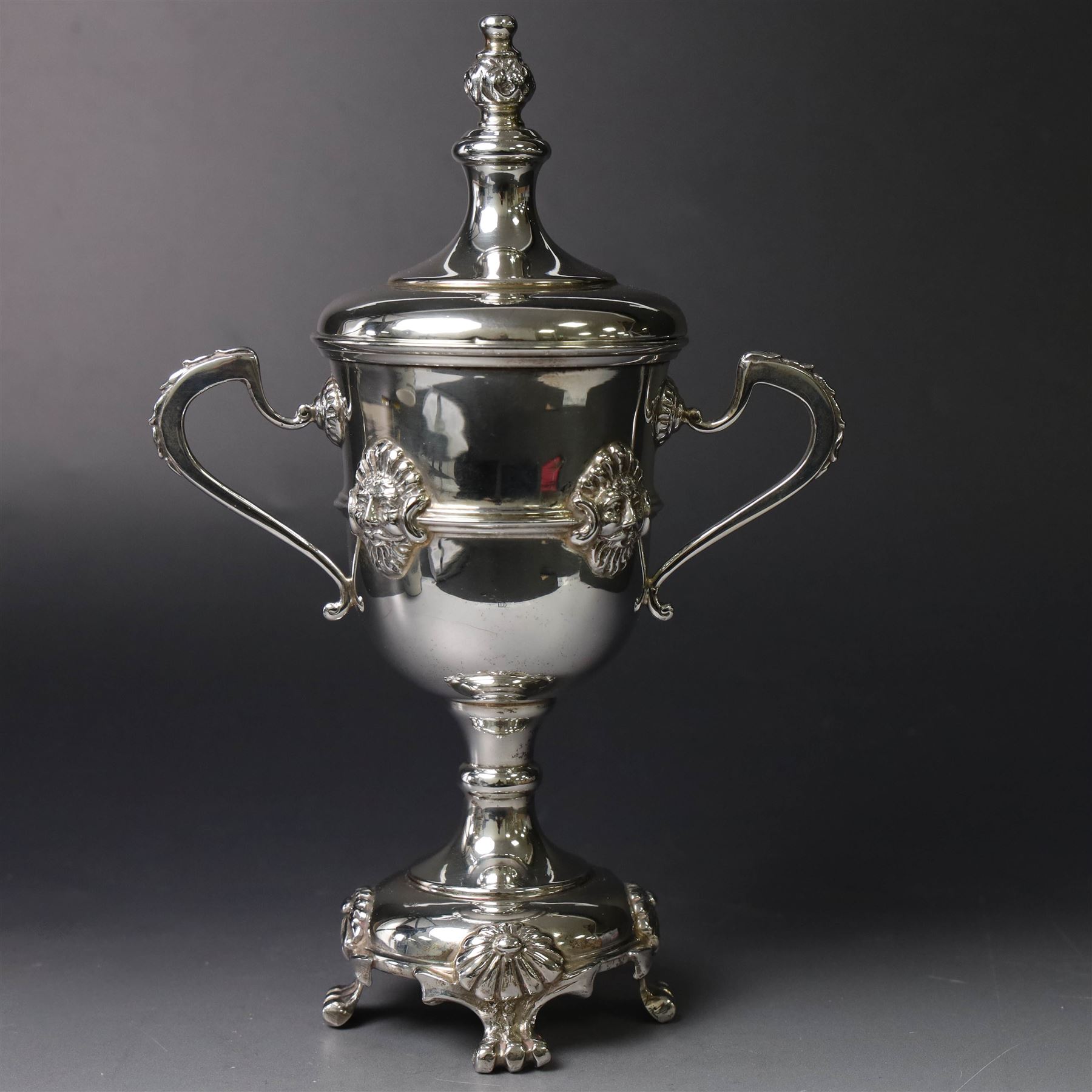 Mid 20th century silver twin handled trophy cup and cover, the bowl with central mask mounted girdle upon a knopped stem and spreading circular foot with flower head mounted paw feet, the tapering stepped cover with leaf moulded knop finial, hallmarked Vaughton & Sons, Birmingham 1938