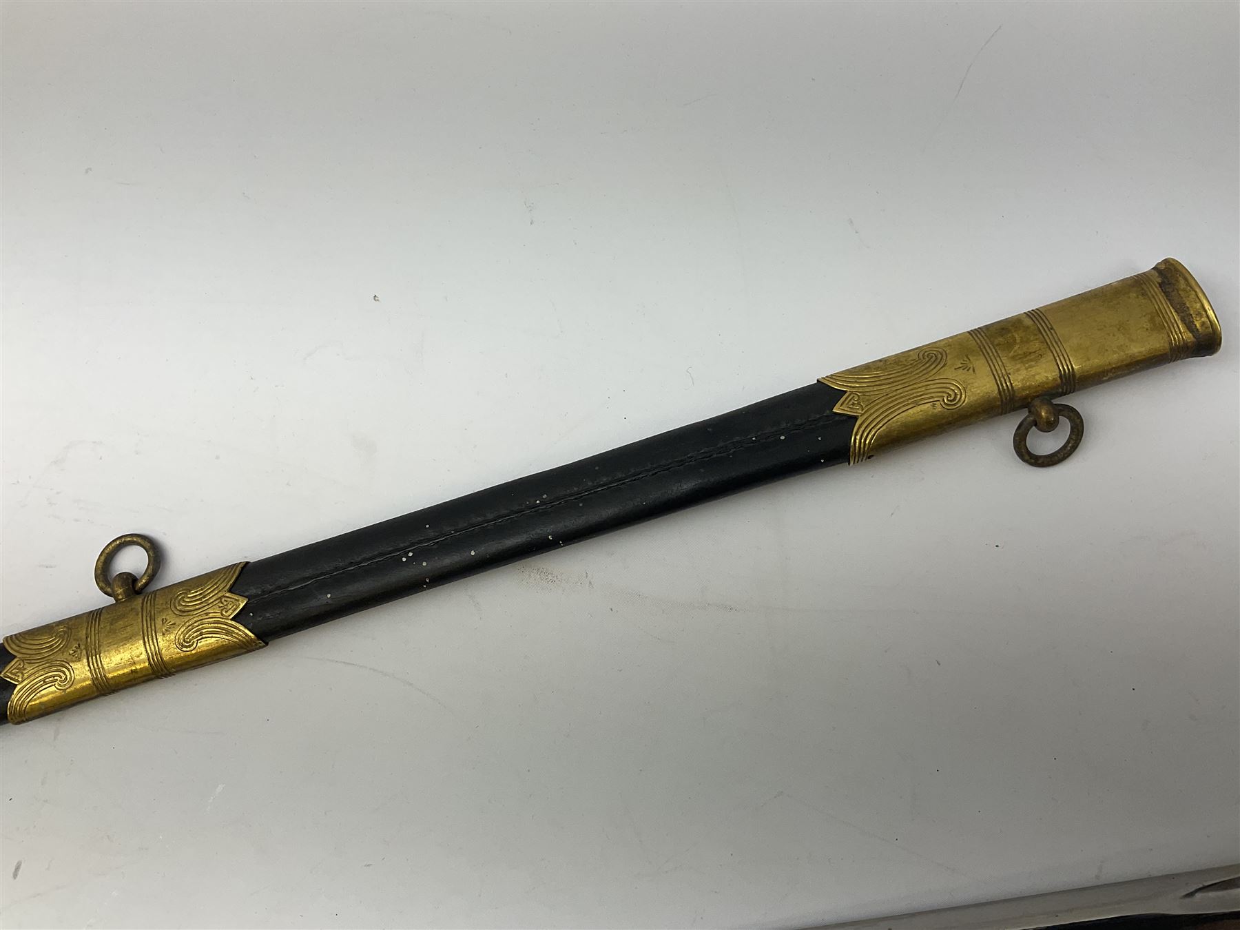 WW1 George V era 1827 Pattern Royal Naval Officer’s sword, the 80cm fullered steel blade decorated with crown, fouled anchor etc and marked Gieves Portsmouth London Edinburgh Devonport to the ricasso, gilded hilt with fouled anchor and crown, wire-bound ray skin grip, lion’s head pommel with mane backstrap, folding/locking langet and full bullion knot; in  leather scabbard having twin brass lockets with hand engraved panels and twin suspension rings L94cm overall. Provenance: By direct family descent from Brian Heathcote HMS Conqueror later Superintendant in the Liverpool Special Constabulary.