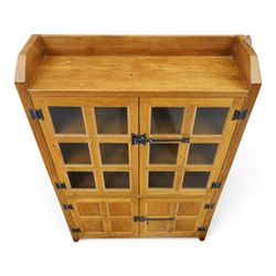 Rabbitman - oak glazed bookcase or display cabinet, lightly adzed rectangular top with raised gallery, twin glazed doors enclosing two shelves, over a pair of panelled cabinet doors with wrought iron fittings, with carved rabbit signature, by Peter Heap of Wetwang