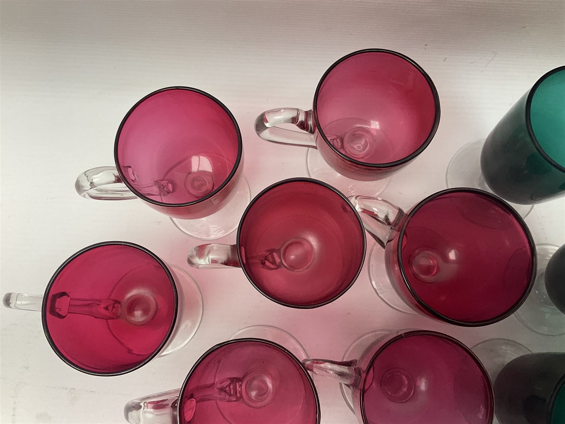 Collection of 19th century coloured glasses, to include nine cranberry glass punch cups, each with clear glass handle and foot and a set of six green glasses, with short clear stems, tallest H10cm