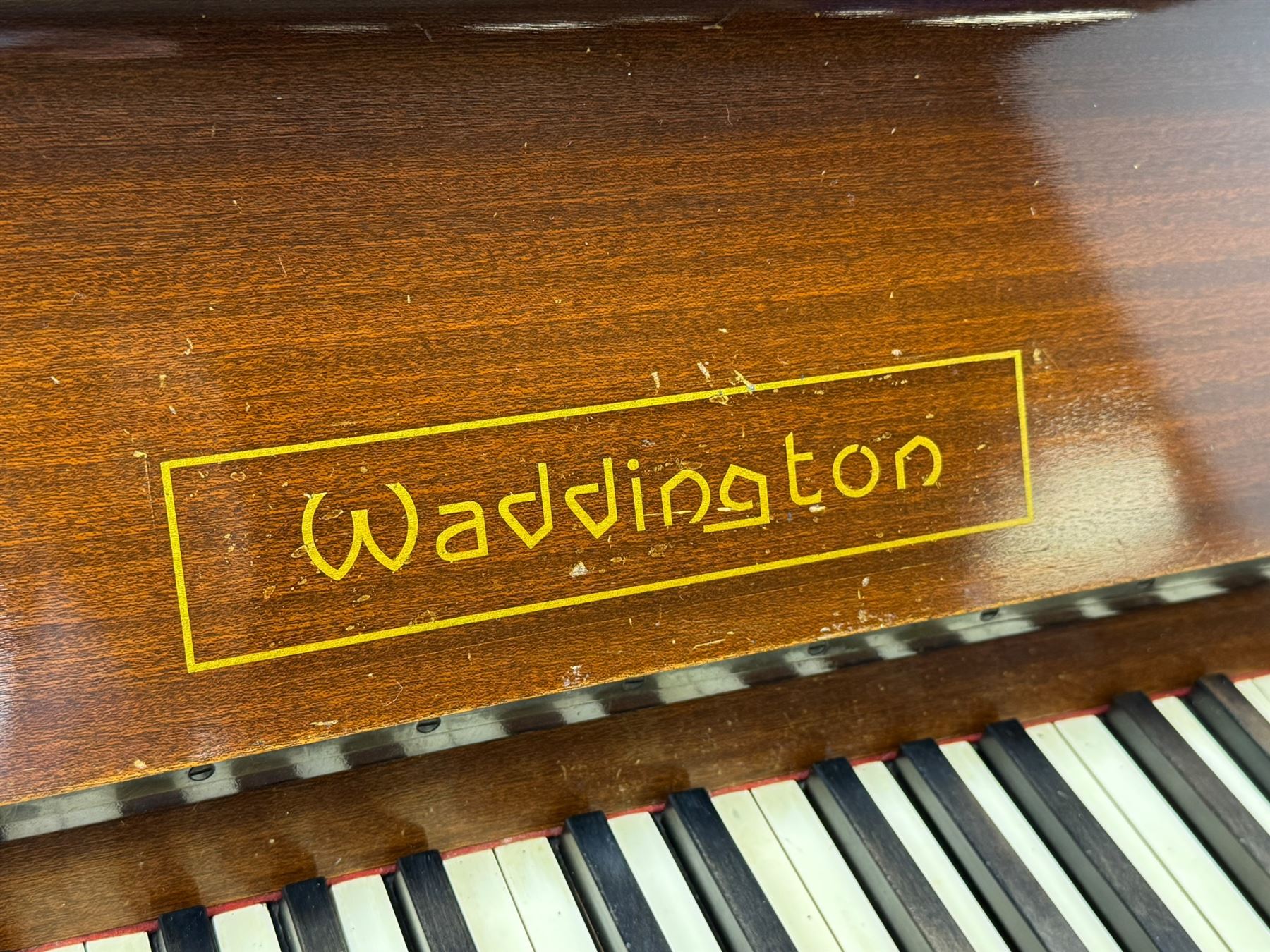 Waddington - Edwardian mahogany upright piano, rectangular top with panelled front, rounded key cover, makers name on fallboard, raised on bracket supports with castors