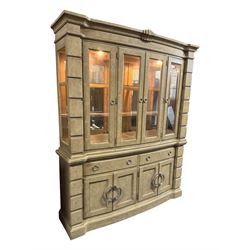 Brunswick - washed oak finish illuminated display cabinet, upper section with four glass-panelled doors enclosing glass shelving, base fitted with two drawers over four paneled cupboard doors, each fitted with distinctive round metal handles, raised on plinth base